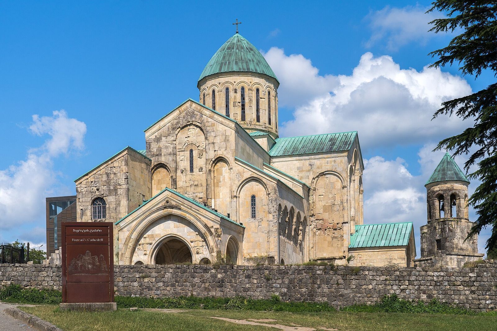 Bagrati Cathedral in Kutaisi, a stone church with a green dome and roofs behind a low stone wall
