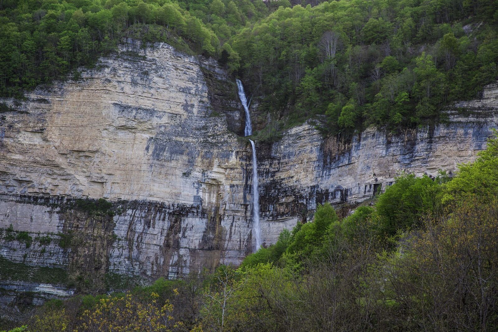 Kinchkha waterfall dropping down a tall limestone cliff in the forest near Okatse Canyon