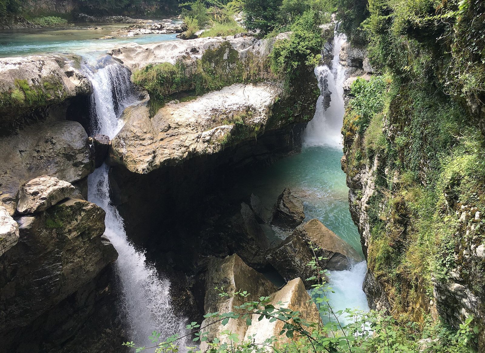Waterfalls dropping into turquoise pools between mossy limestone walls in Martvili Canyon