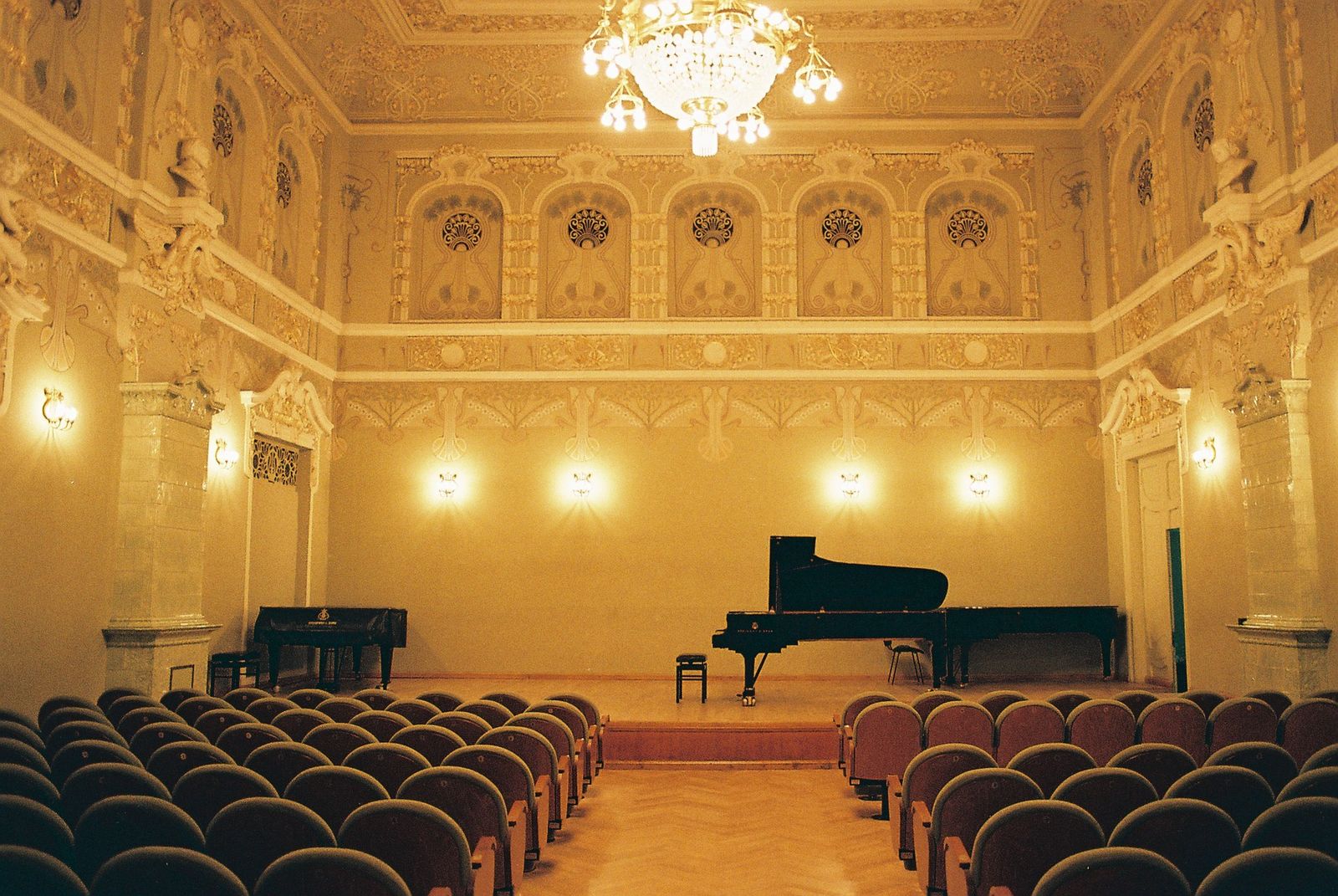 A concert hall at the Tbilisi State Conservatoire with a grand piano on stage, a crystal chandelier and ornate gilded walls