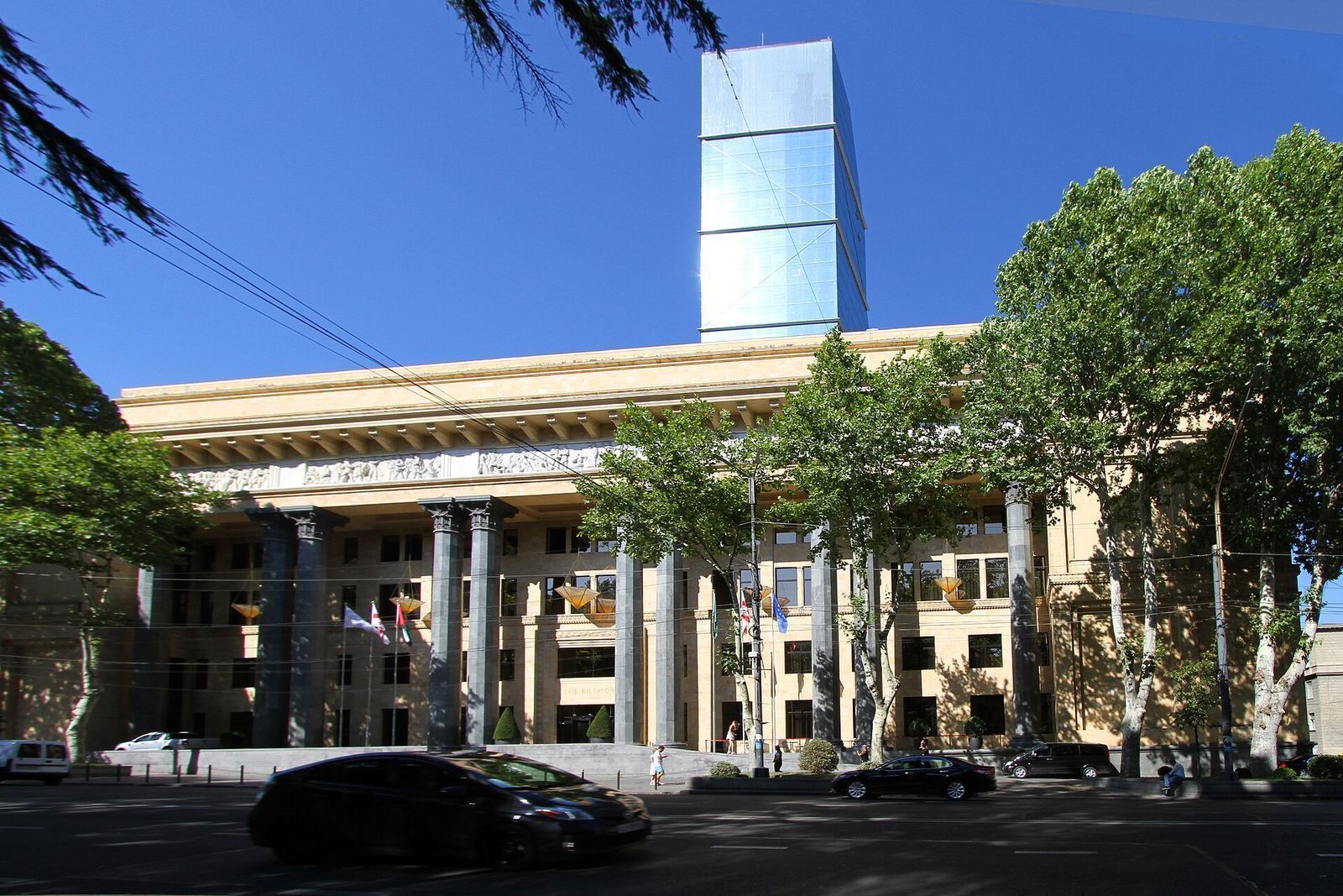 The Biltmore Hotel on Rustaveli Avenue, the former IMELI building, with its dark stone columns and the glass hotel tower rising behind it