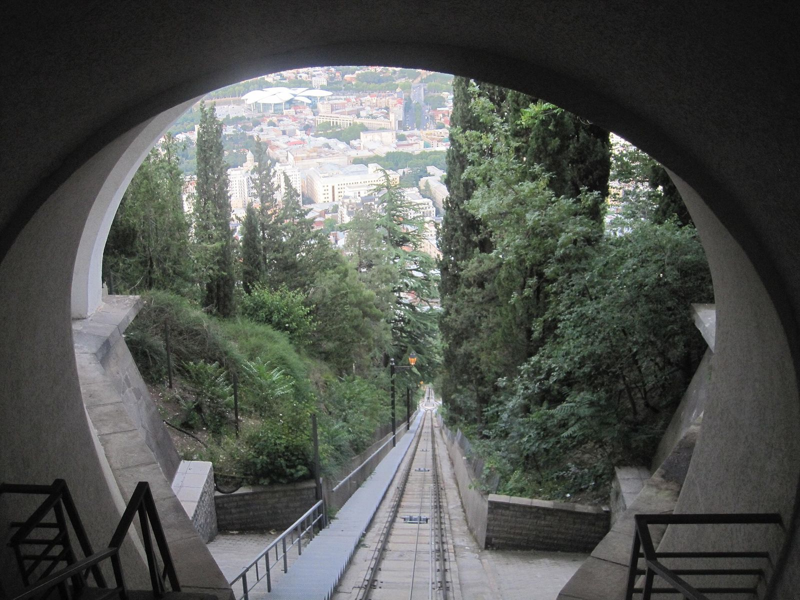 The Tbilisi funicular track running down Mtatsminda between trees, seen through a station arch