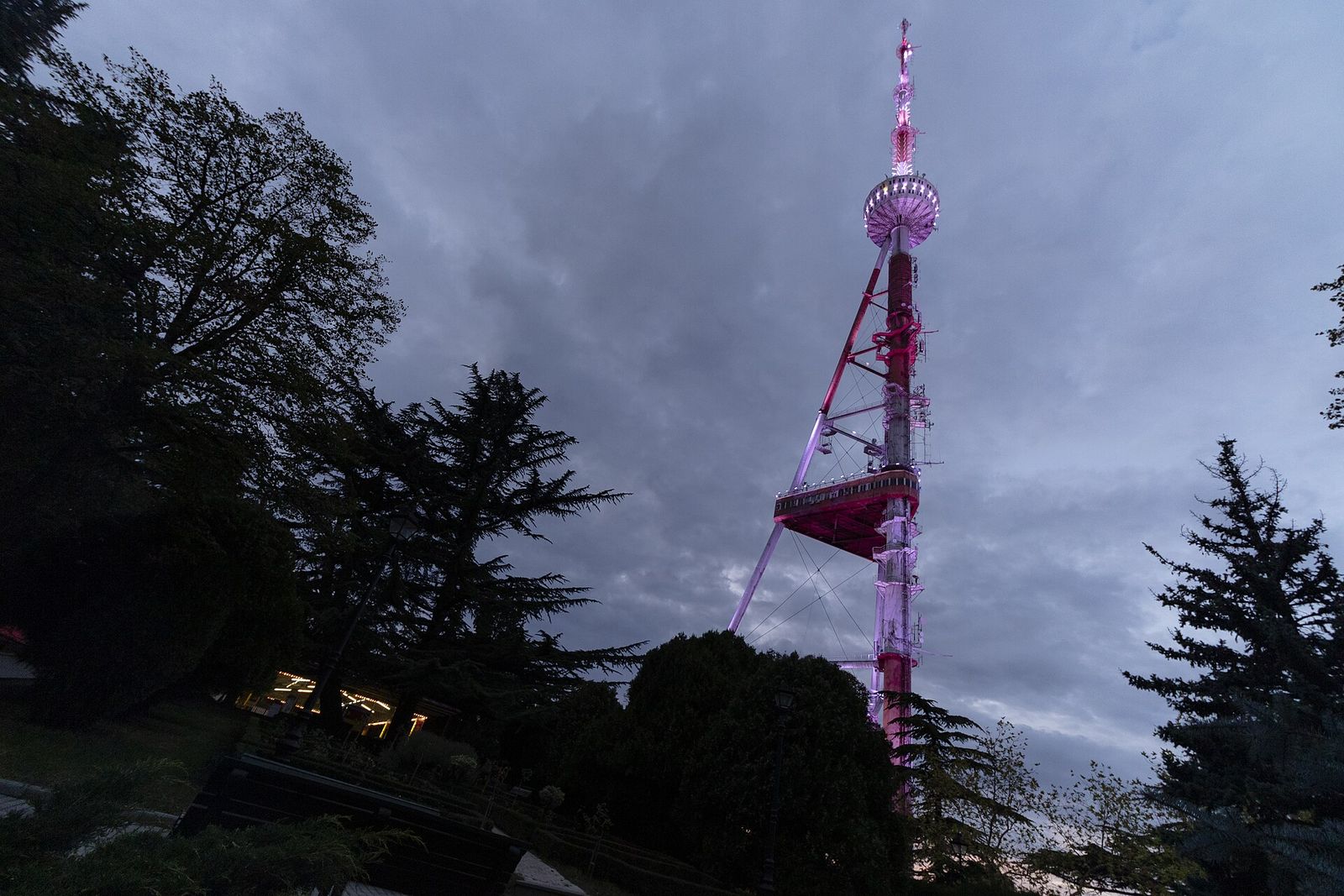 The Tbilisi TV tower on Mtatsminda lit up at dusk, seen from the park below