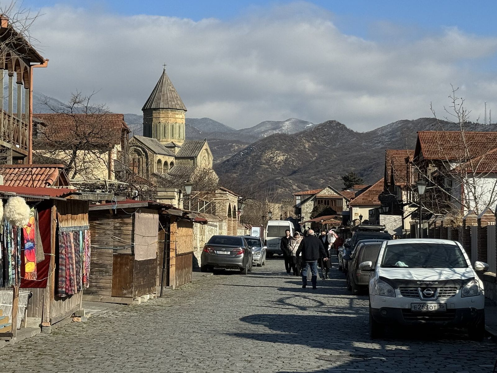 Souvenir stalls and wooden balconies along the cobbled old town street in Mtskheta, with the dome of Svetitskhoveli Cathedral behind