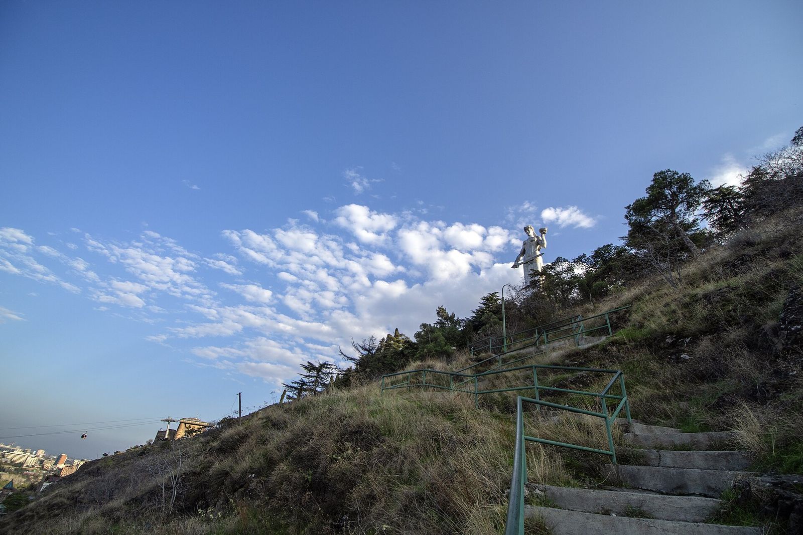 Stone stairs climbing the grassy ridge to the Mother of Georgia statue above Tbilisi
