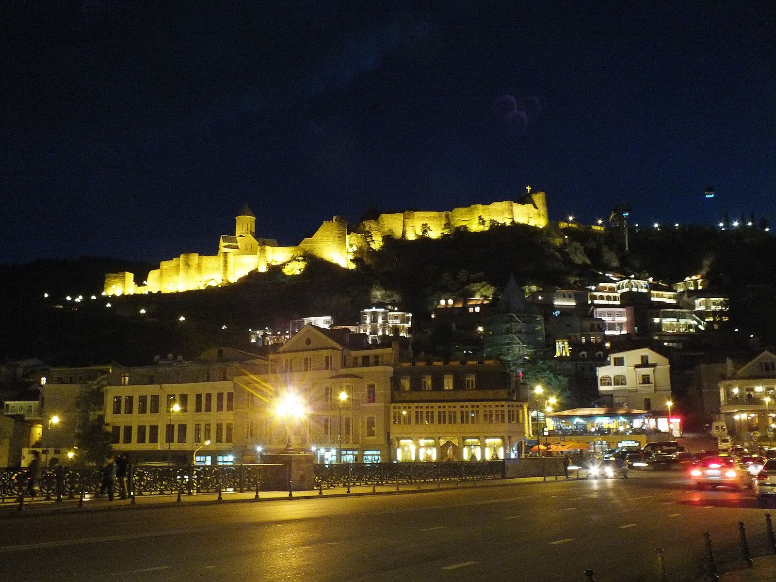 Narikala's floodlit walls and St Nicholas Church above the lit-up Old Town at night, seen from the Metekhi Bridge