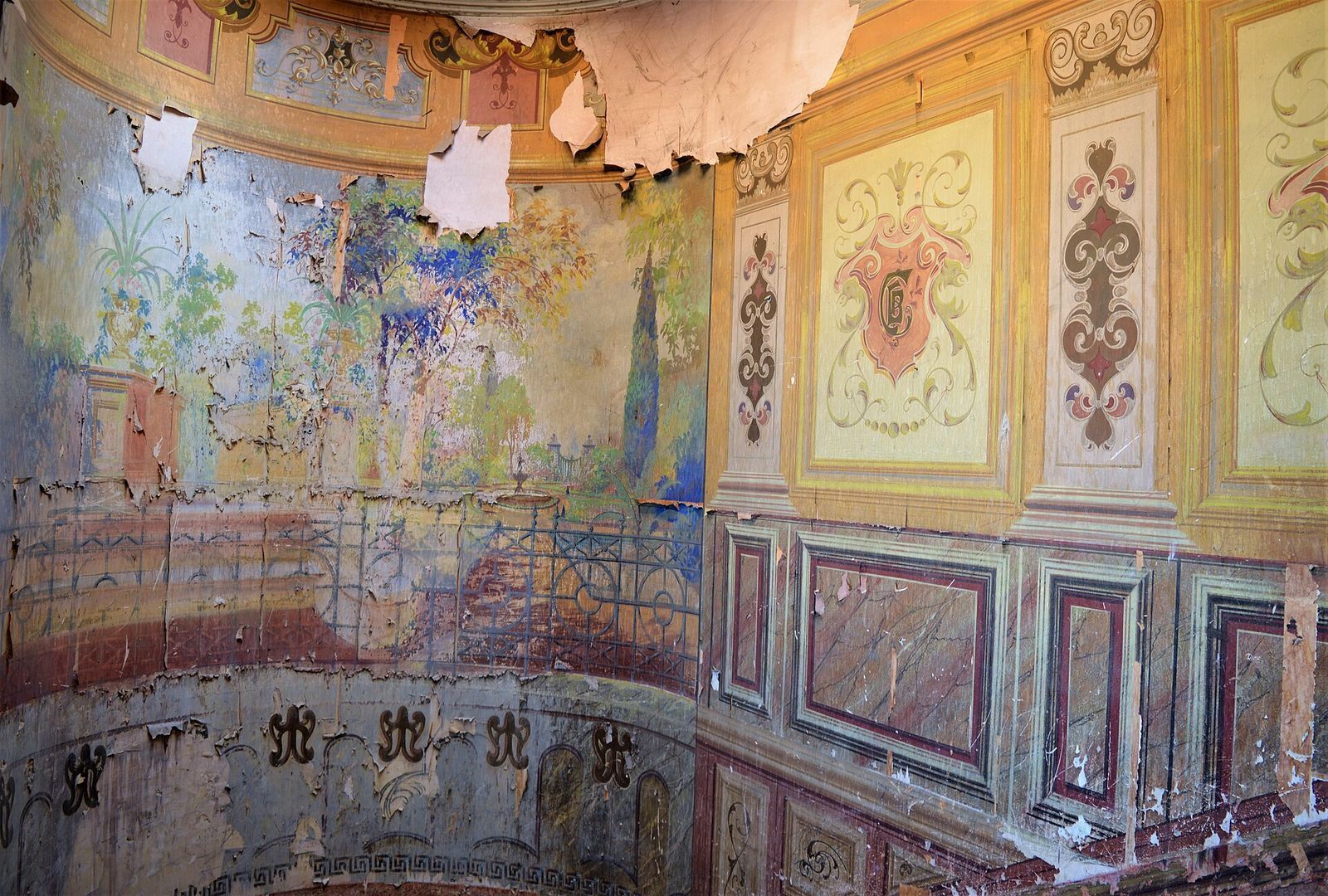 A peeling garden mural with a painted railing and faded painted panels on the walls of the entrance hall at 18 Galaktion Tabidze Street in Sololaki