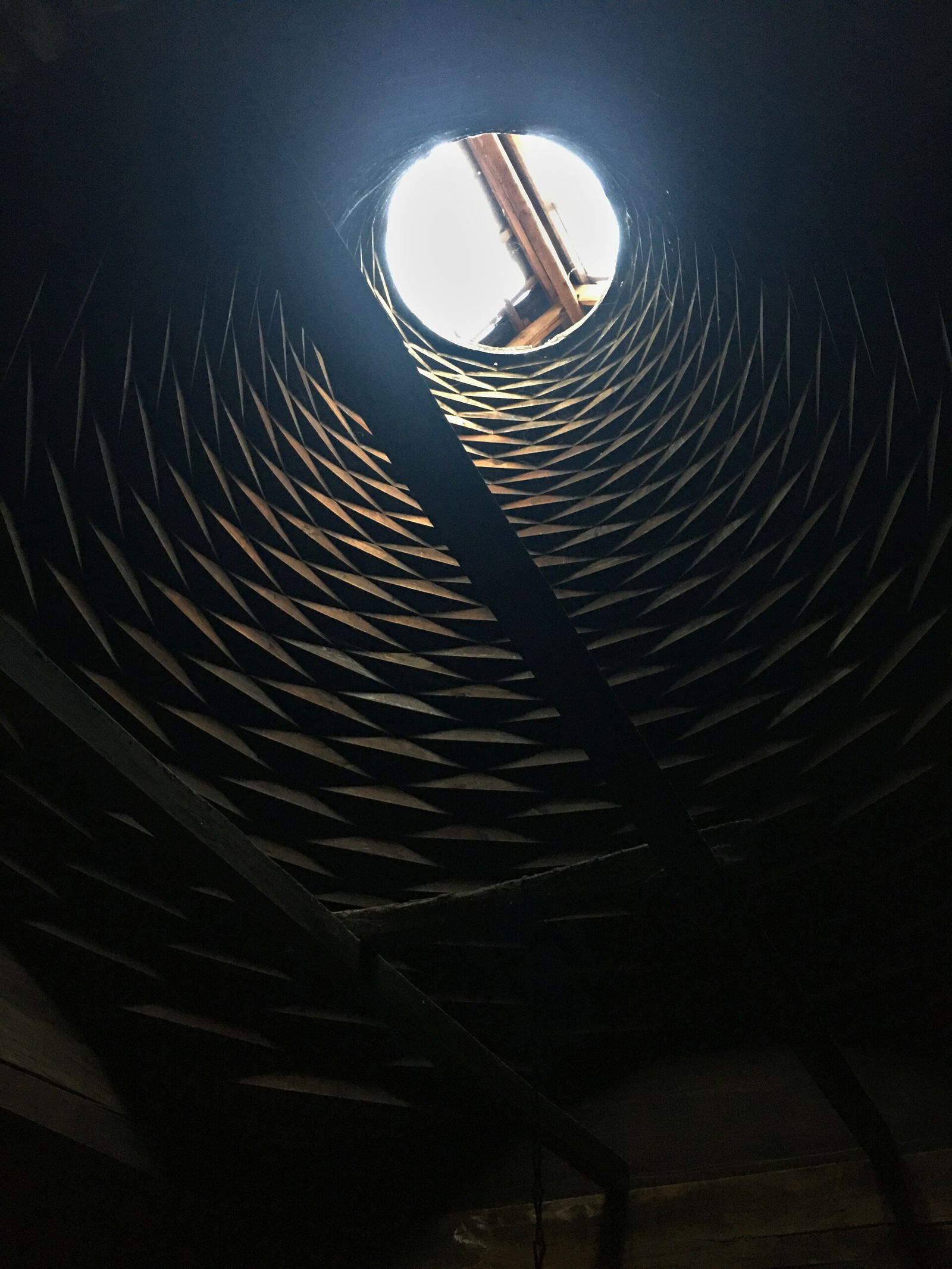 Looking up into the stepped wooden ceiling of a darbazi house at the Open Air Museum of Ethnography, rising in rings to a single round smoke hole