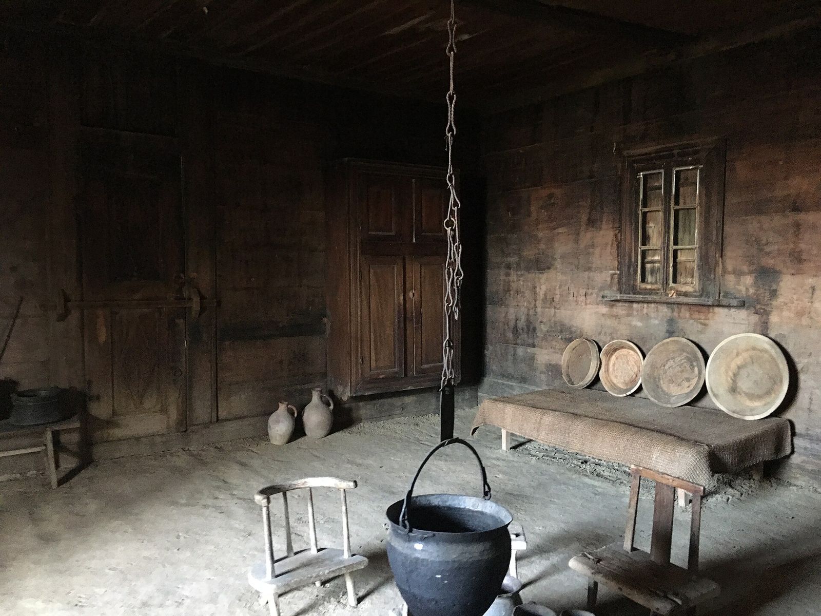 Inside a village house at the Open Air Museum of Ethnography: a cauldron hanging over the hearth, wooden dishes, clay jugs and a low stool