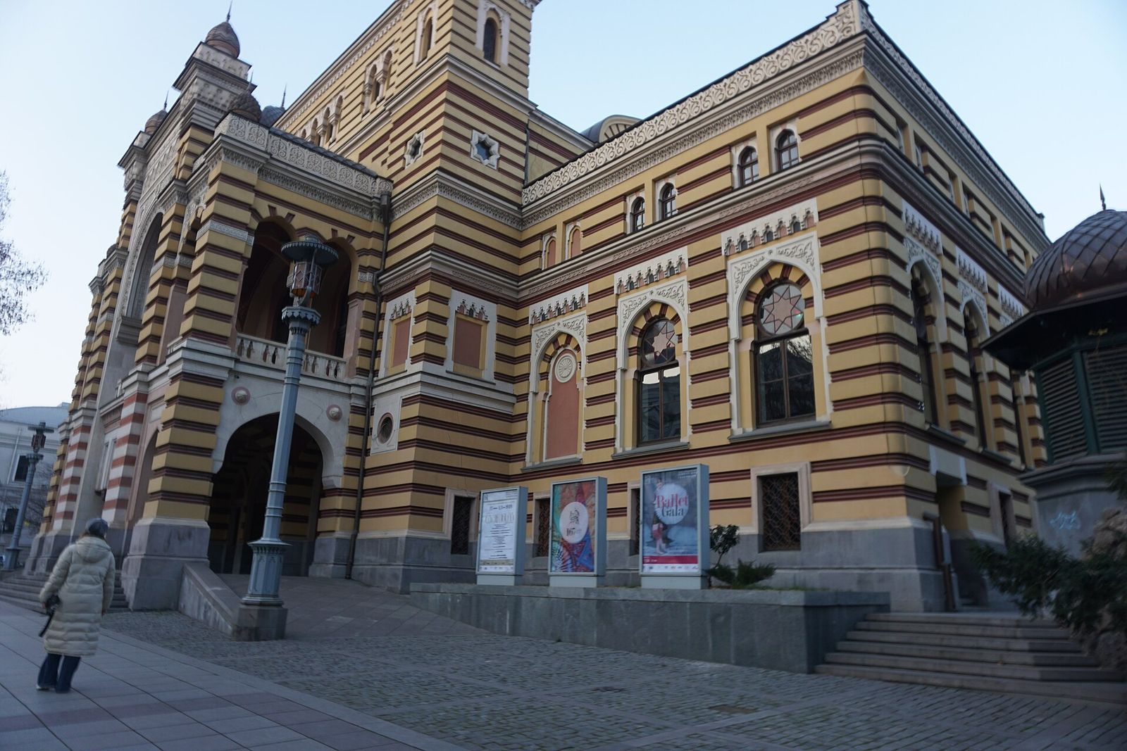 The entrance of the Tbilisi Opera and Ballet Theatre with performance posters on stands in front of the striped facade