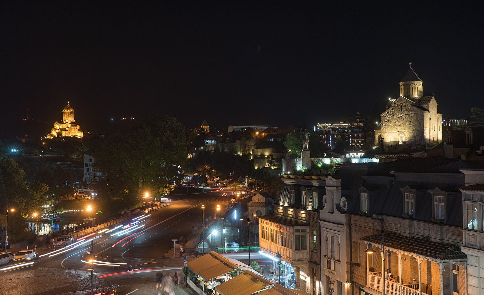 Old Tbilisi at night, with Metekhi Church lit up on the cliff and Sameba Cathedral glowing on the hill behind