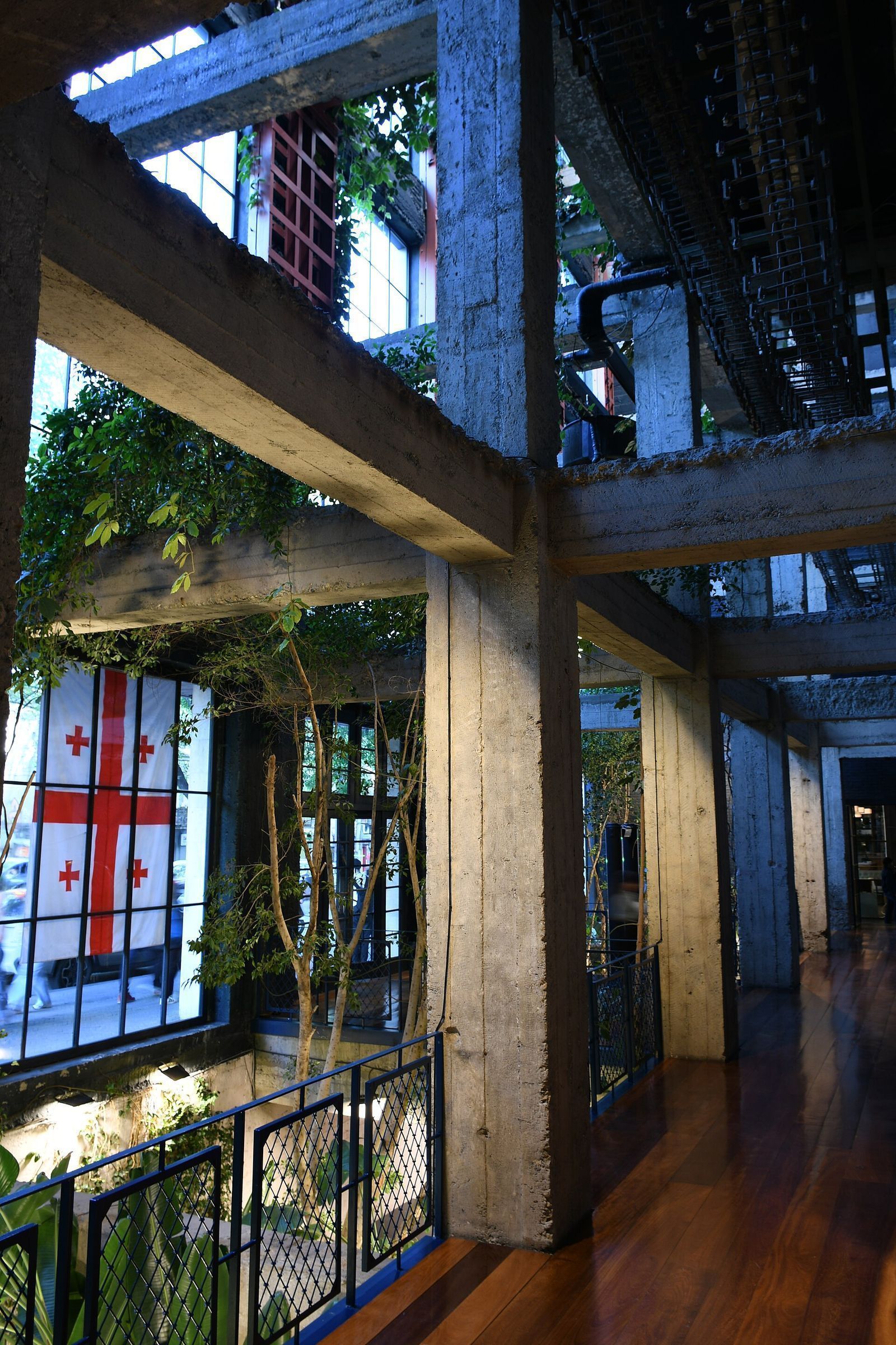 Raw concrete beams and columns, climbing plants and a Georgian flag in the atrium of Stamba Hotel, the former Soviet publishing house