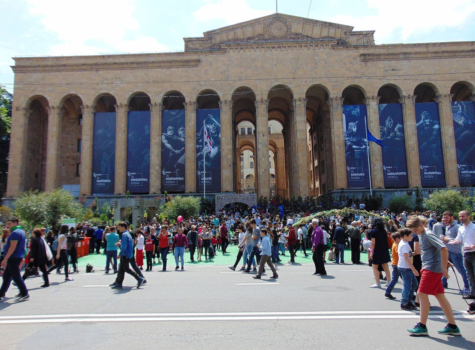 Crowds on Rustaveli Avenue in front of the arched facade of the Parliament building during Independence Day celebrations