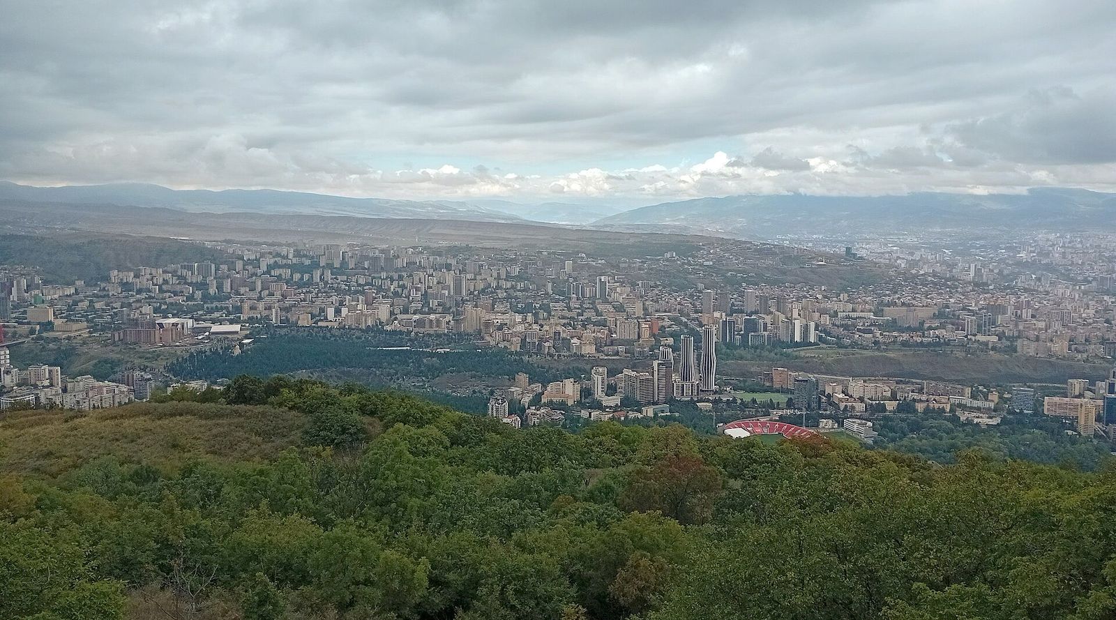 The apartment blocks and towers of Saburtalo spread across the valley, seen from the wooded ridge above the Open Air Museum of Ethnography