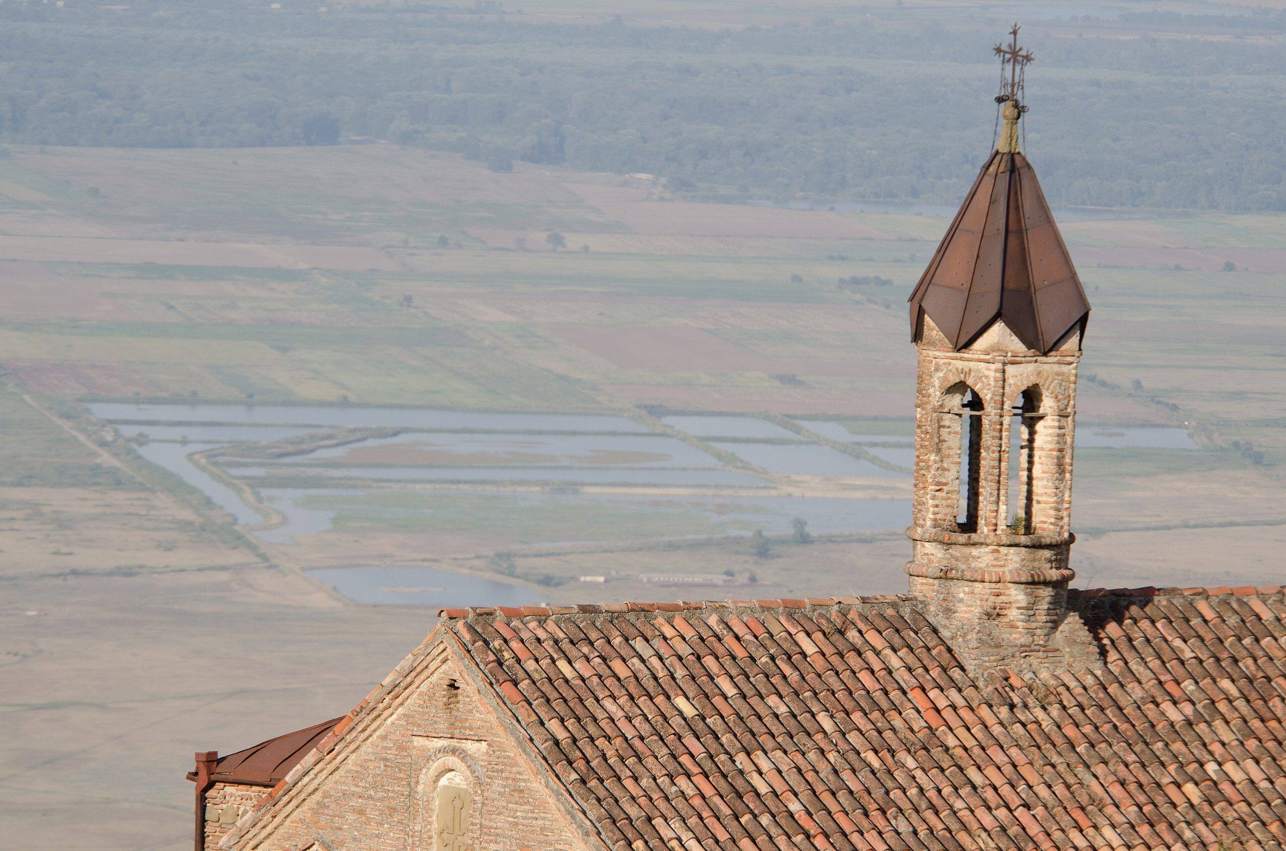 A brick bell tower and tiled church roof in Sighnaghi, high above the flat fields of the Alazani Valley