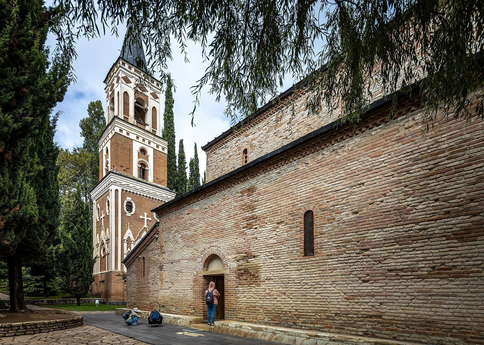 The brick church of Bodbe Monastery and its tall white and brick bell tower among cypress trees