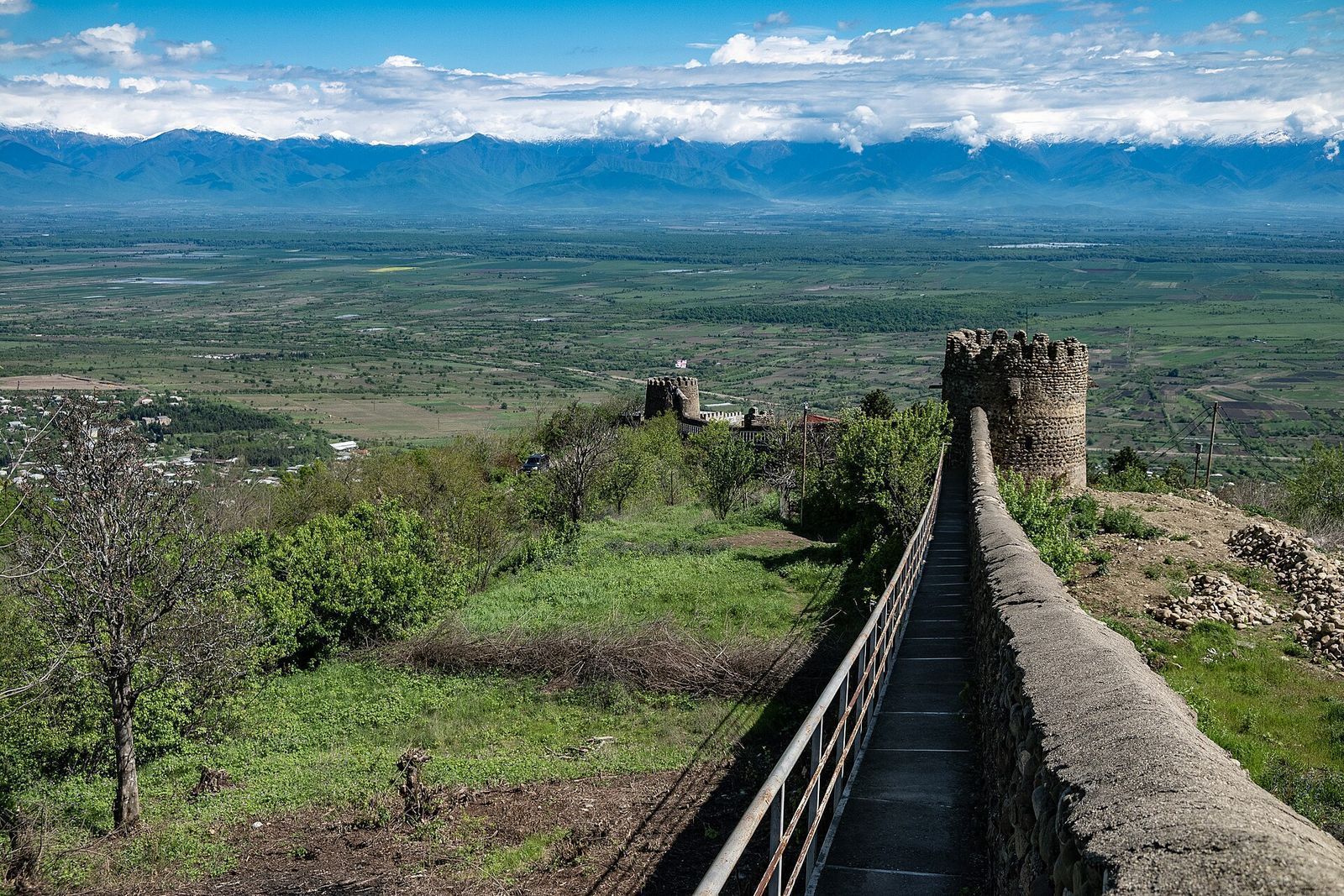 The walkway along the fortress wall of Sighnaghi, with a round tower and the Alazani Valley and Caucasus mountains beyond