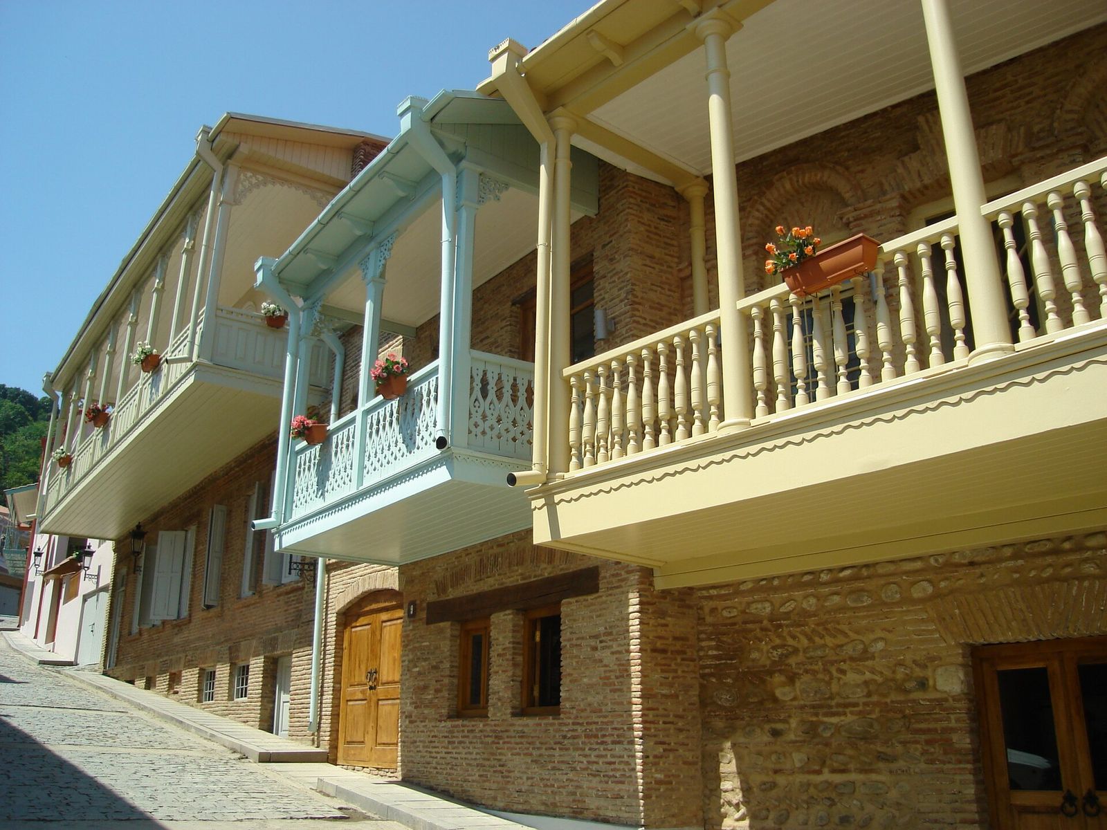 Carved wooden balconies painted cream, pale blue and off-white on 19th-century brick houses along a cobbled street in Sighnaghi