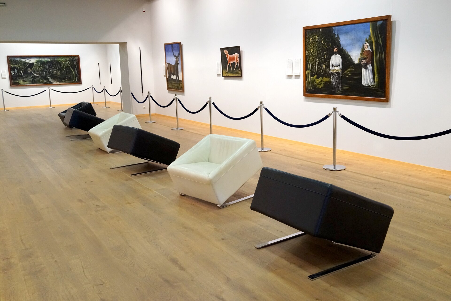 A gallery of Niko Pirosmani paintings in the Sighnaghi National Museum, with a stag, a deer and a couple in a vineyard on the white walls