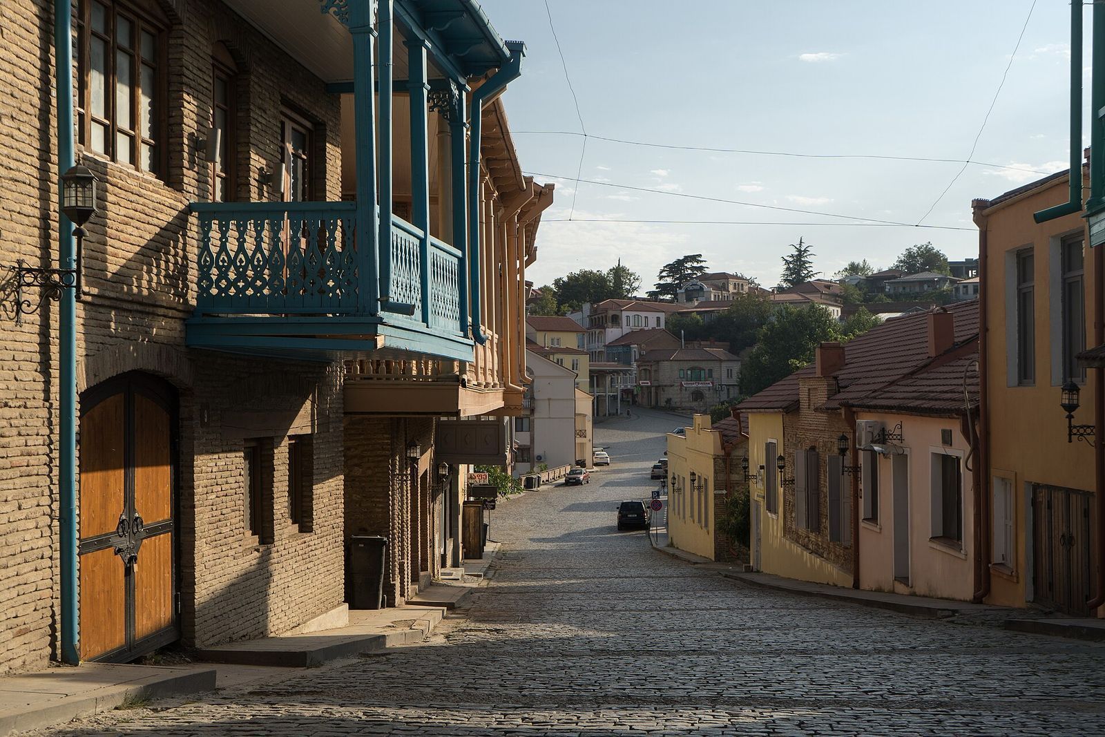 A cobbled street in Sighnaghi's old town running downhill between brick houses with blue wooden balconies