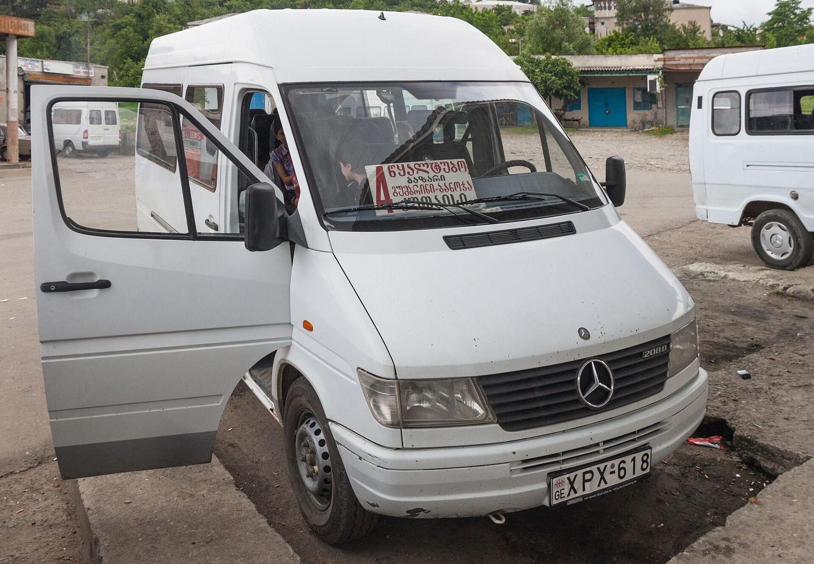 A white Mercedes Sprinter marshrutka with its route sign in the windshield, waiting at a bus station in western Georgia