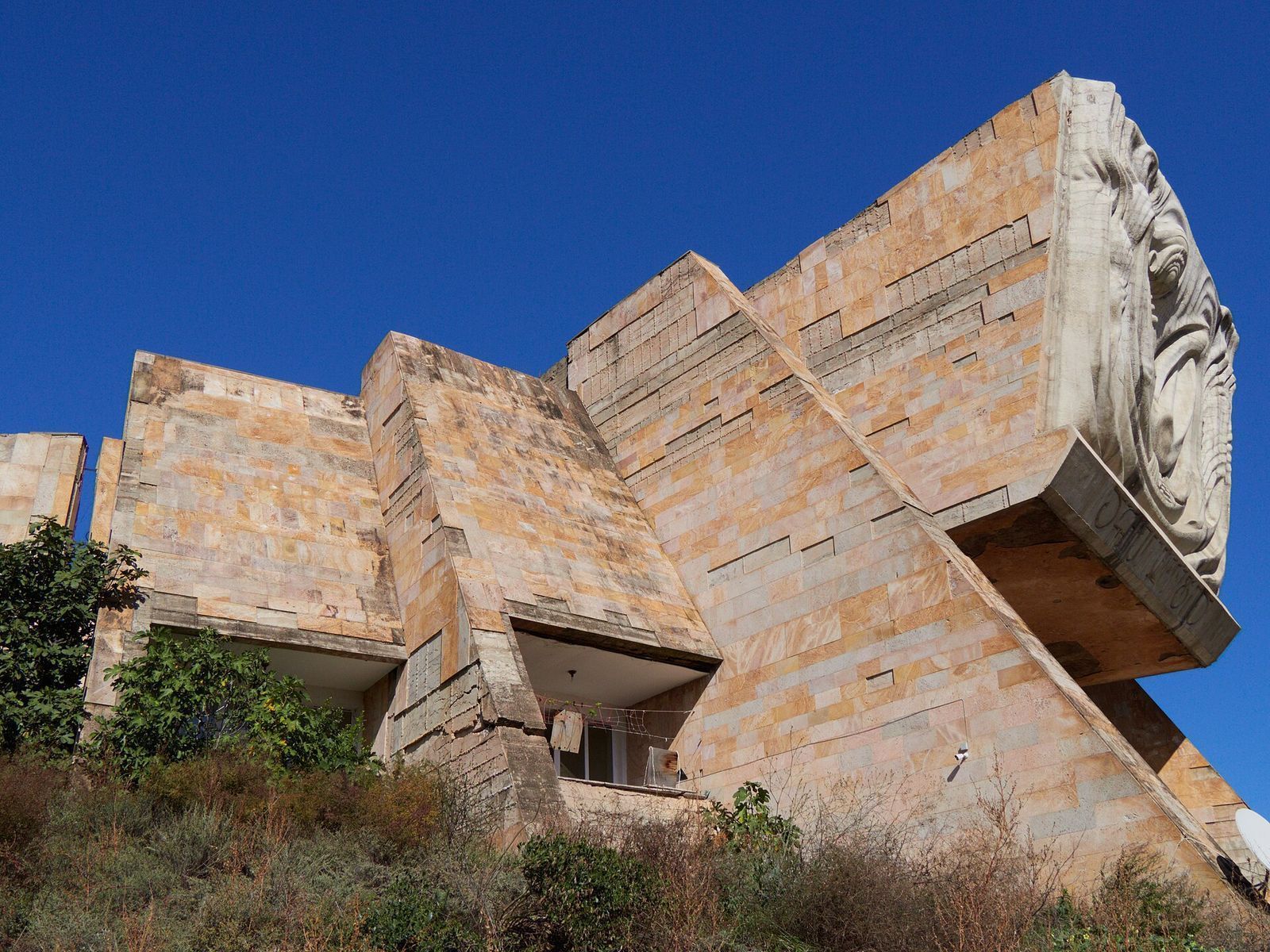 The stone-clad, angular walls of the Tbilisi Archaeological Museum in Dighomi, with the relief of a curled human figure jutting out above the main entrance
