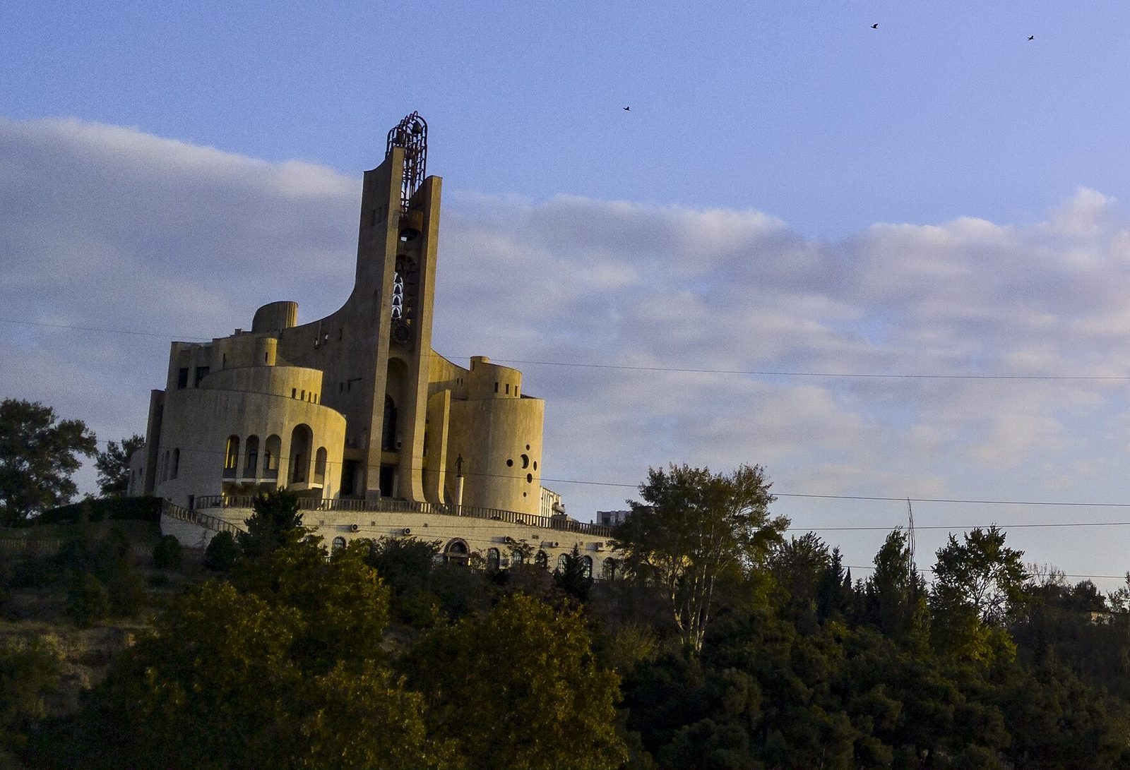 The Palace of Rituals on its wooded hill above Ortachala, its tall spire and rounded towers catching the evening sun