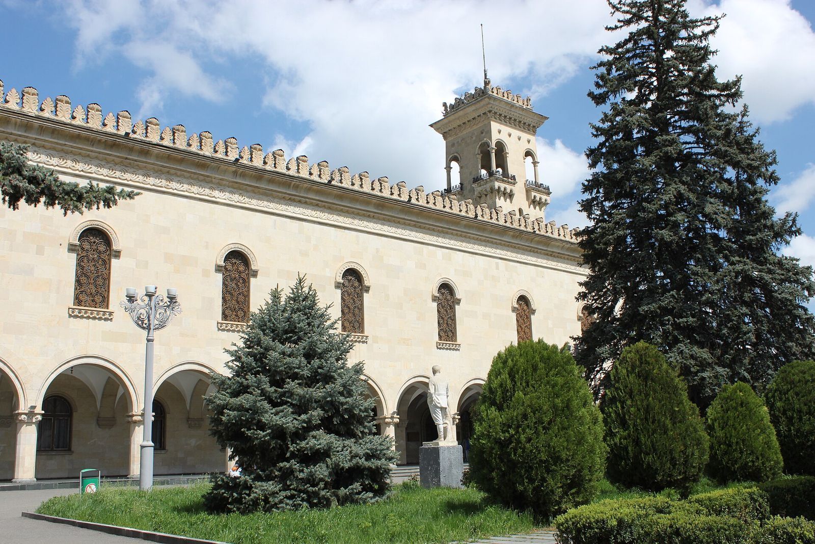The arcaded stone facade and tower of the Stalin Museum's main building in Gori, behind fir trees