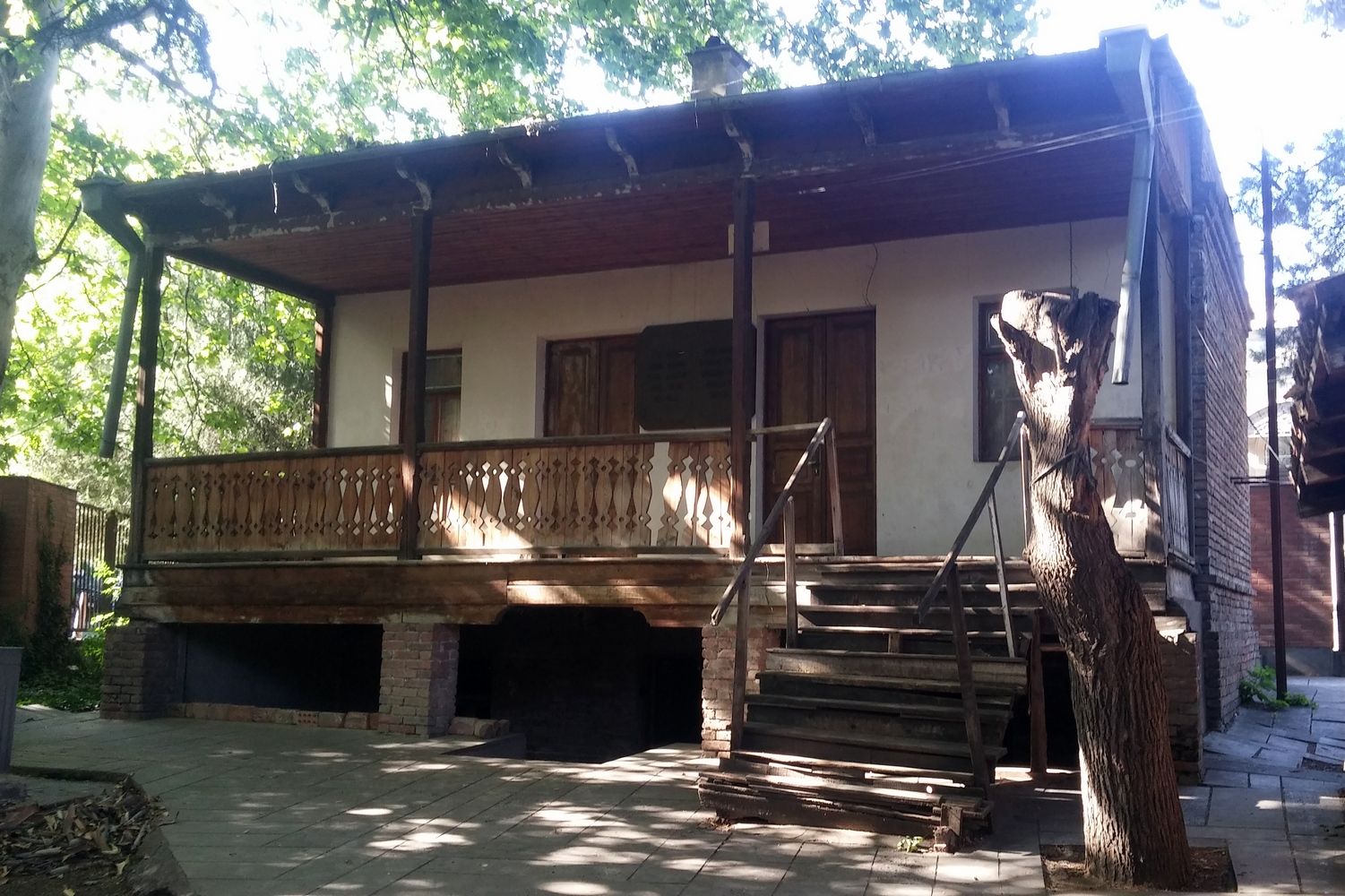 The small wooden house of Stalin's Underground Printing House museum in Avlabari, with its carved porch and wooden steps in a shaded courtyard