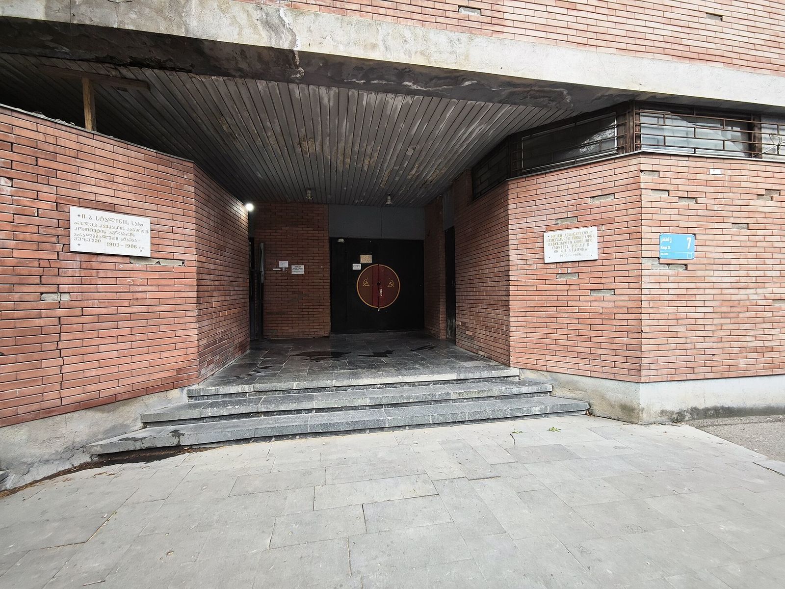 The entrance of the Underground Printing House Museum at 7 Kaspi Street, a brick passage with two plaques and a black door painted with a hammer and sickle