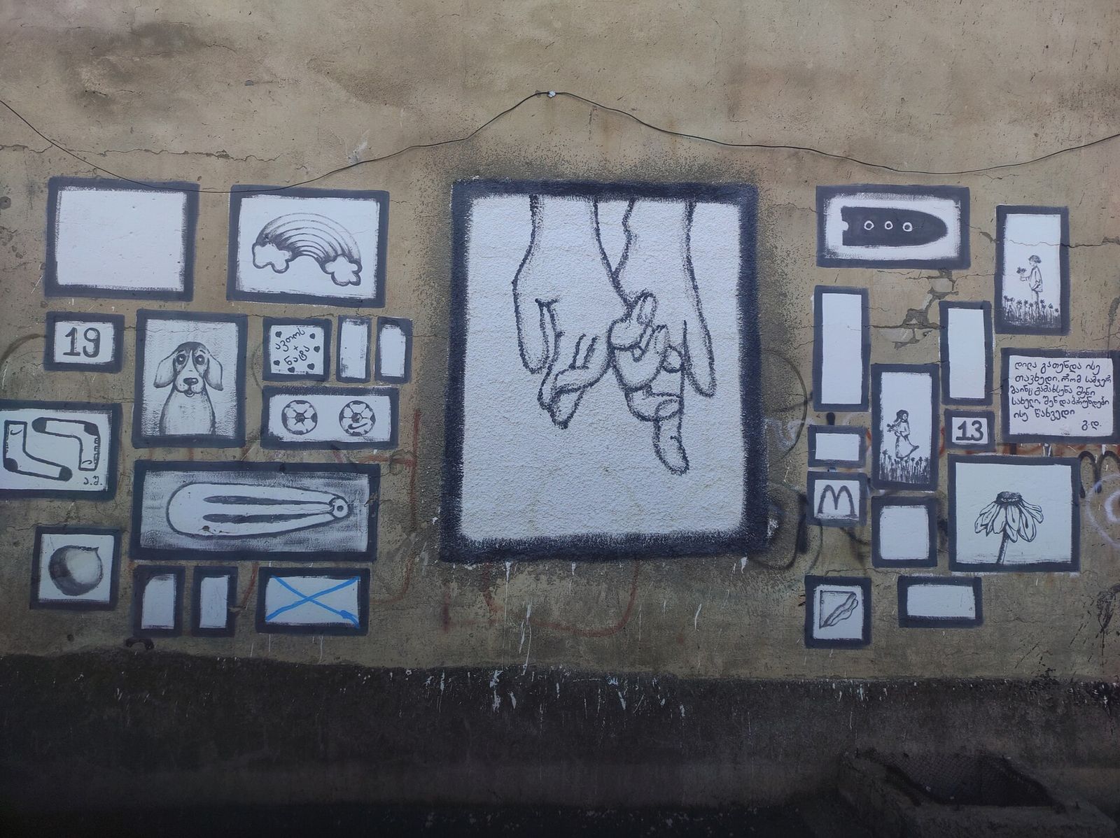 A wall in Orkhevi painted with a gallery of small black and white framed drawings around a central picture of two clasped hands