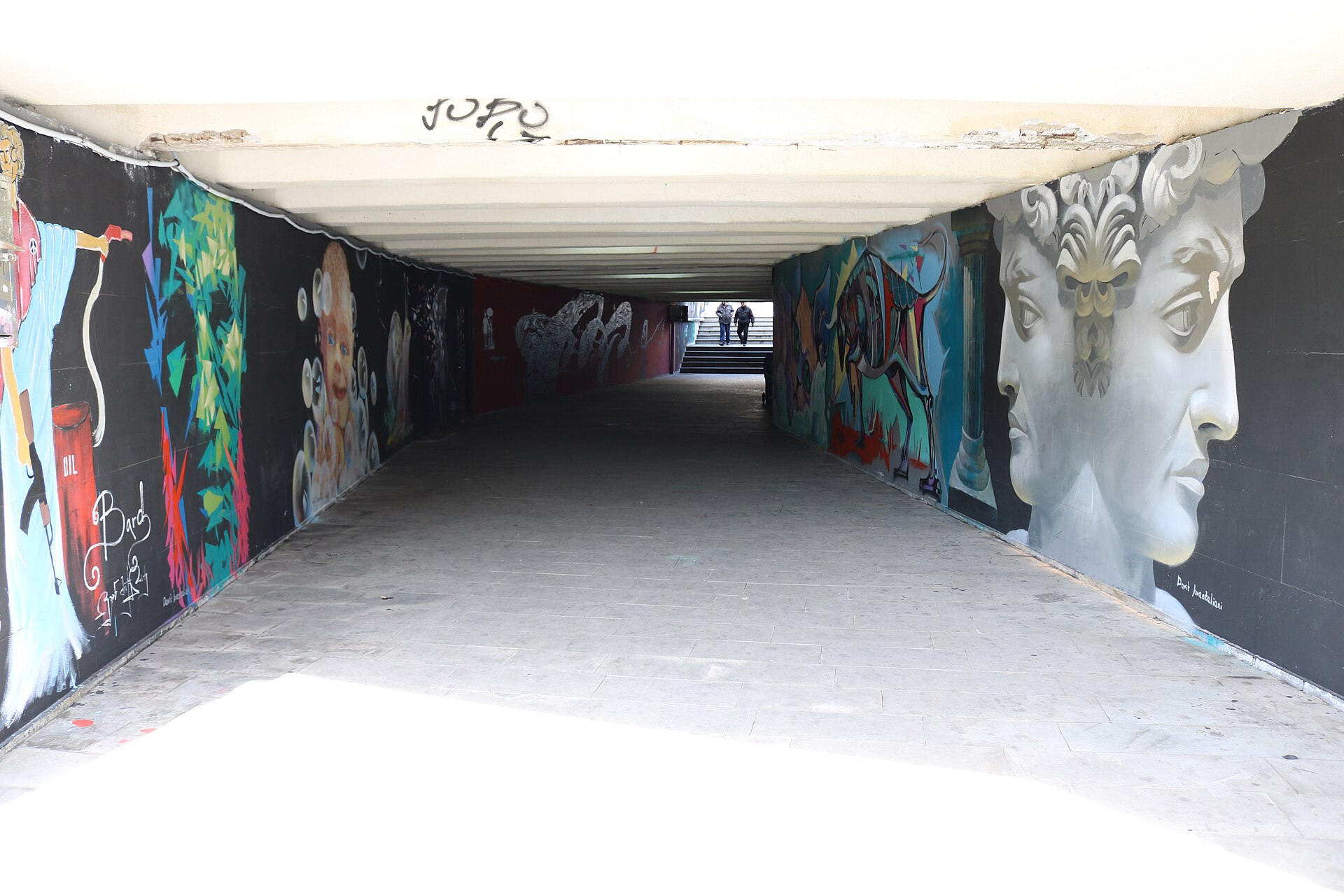 Murals lining both walls of the Heroes Square pedestrian underpass, including a giant painted classical head