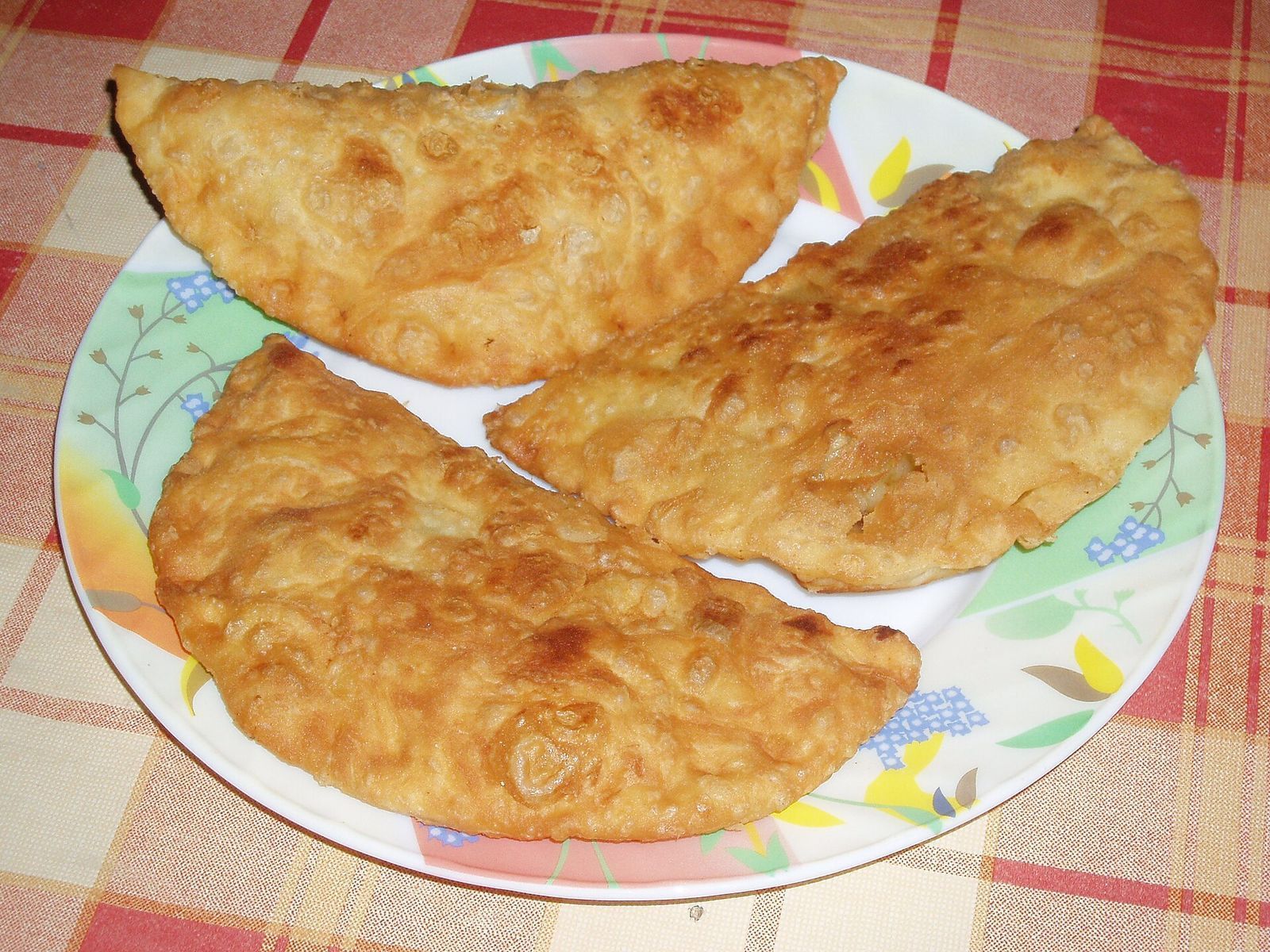 Three chebureki, half-moon pastries fried crisp and blistered, on a plate