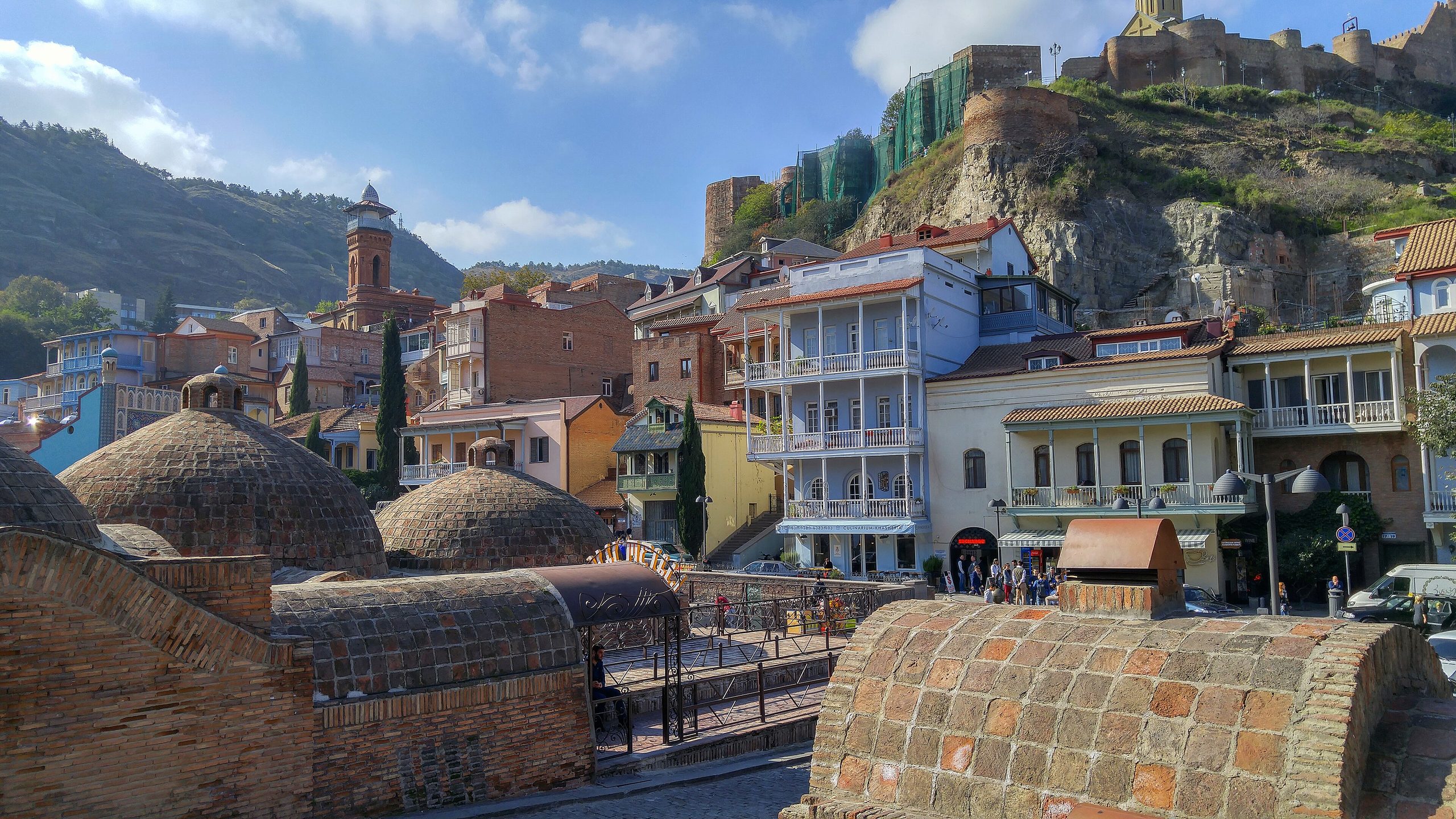 The brick domes of the Abanotubani bathhouses, with the red-brick minaret of the Jumah Mosque and Narikala Fortress on the ridge behind