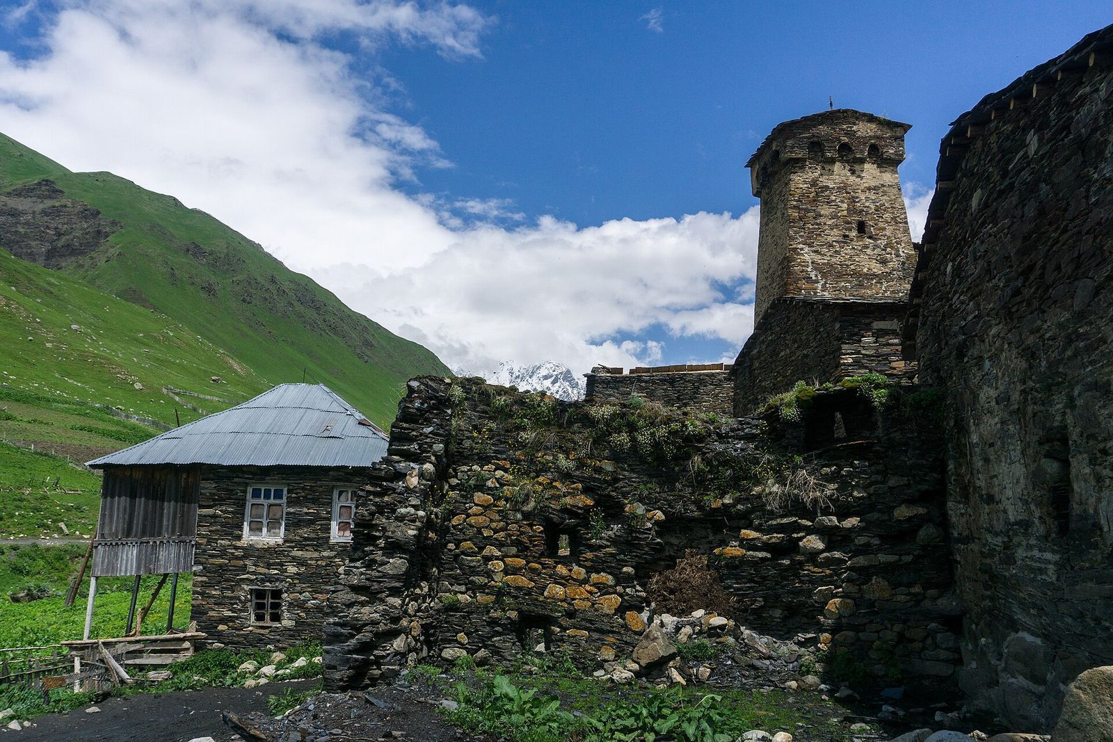 A medieval Svan defense tower and slate stone houses in Ushguli under green mountain slopes