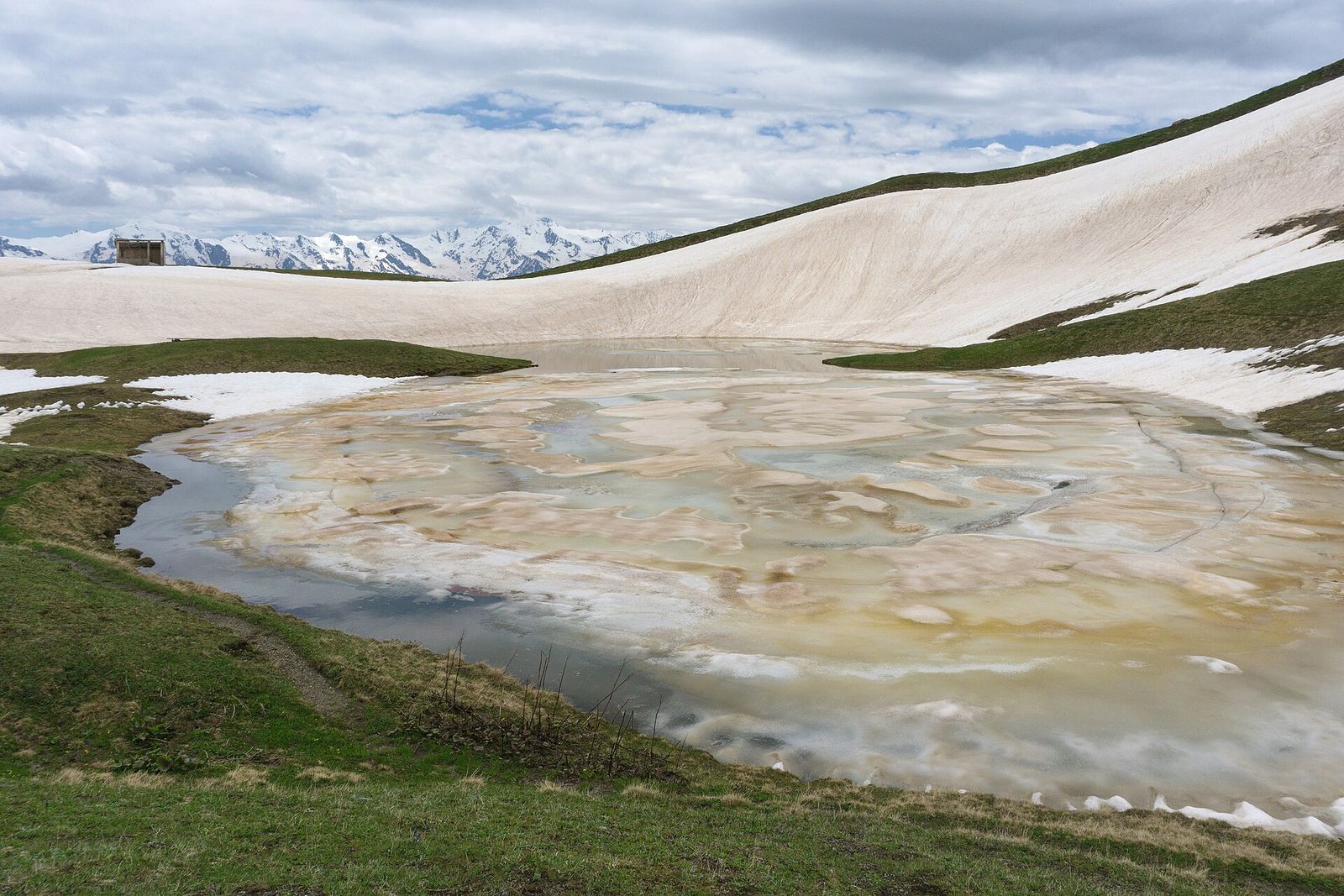 A Koruldi lake still half frozen in early summer above Mestia, with the snowy peaks of the Caucasus behind