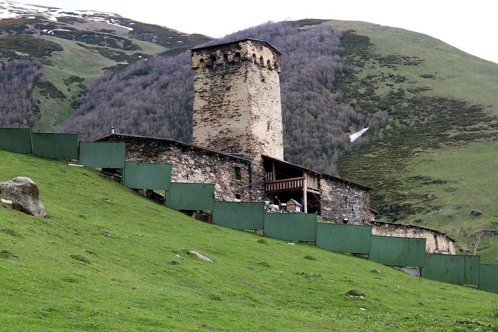 The tower and stone buildings of the Lamaria Church complex on the green slope above Ushguli