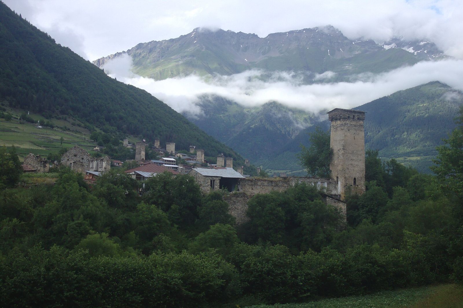 Medieval Svan defense towers rising above the houses of Mestia, with cloud on the mountains behind
