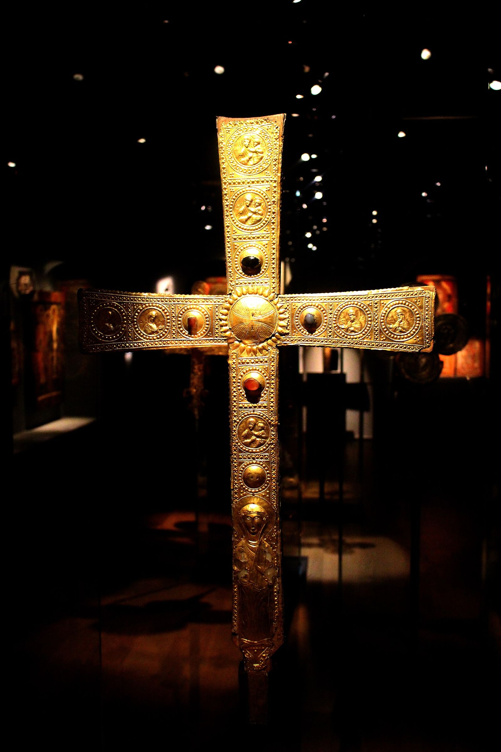 A gilded medieval processional cross set with stones, on display in the dark galleries of the Svaneti Museum in Mestia