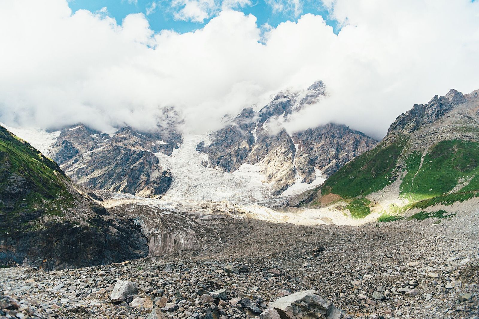 The Shkhara Glacier spilling down from the clouded wall of Shkhara, with a wide gray moraine at its foot