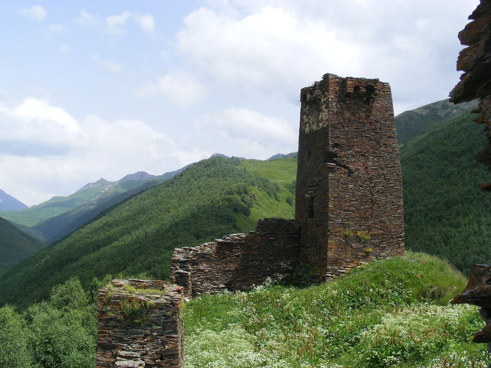 The ruined Queen Tamar tower and its broken stone walls on the green hill above Chazhashi in Ushguli