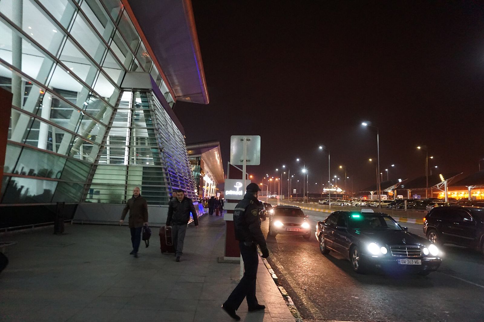 A taxi pulling up to arriving passengers outside the arrivals hall at Tbilisi International Airport at night