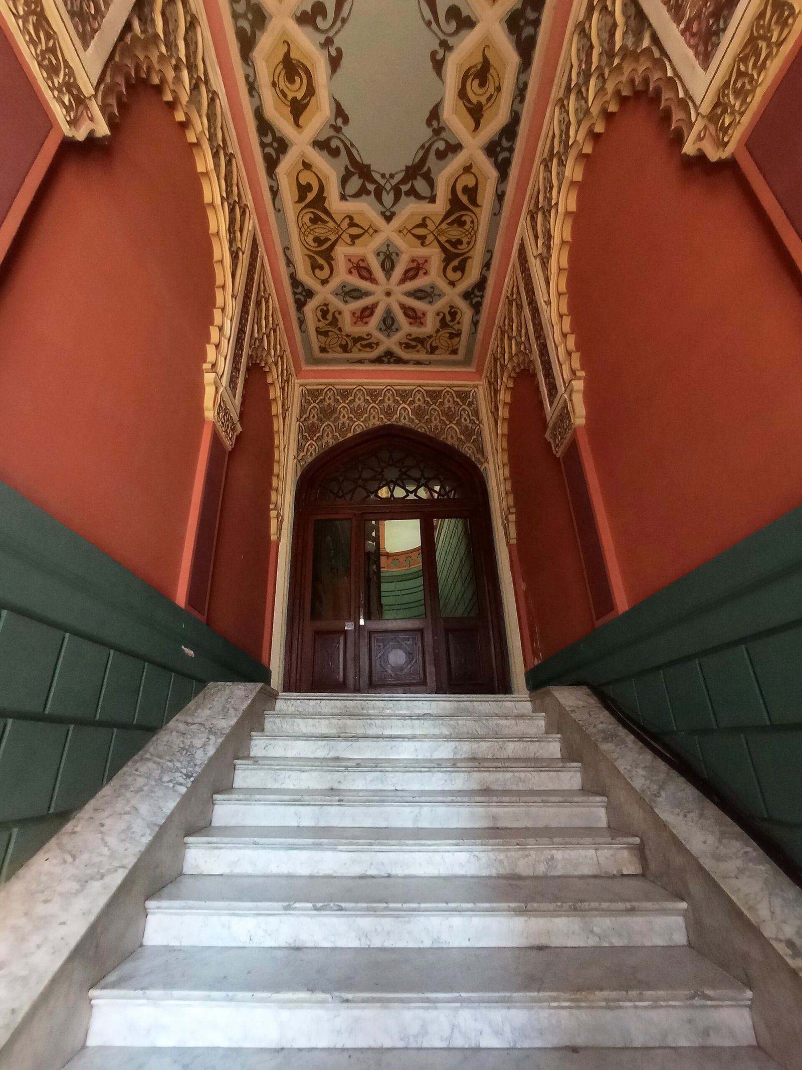 The Persian-style painted entrance hall at 17 Ivane Machabeli Street in Sololaki, with red walls, carved arches, a painted ceiling and marble stairs