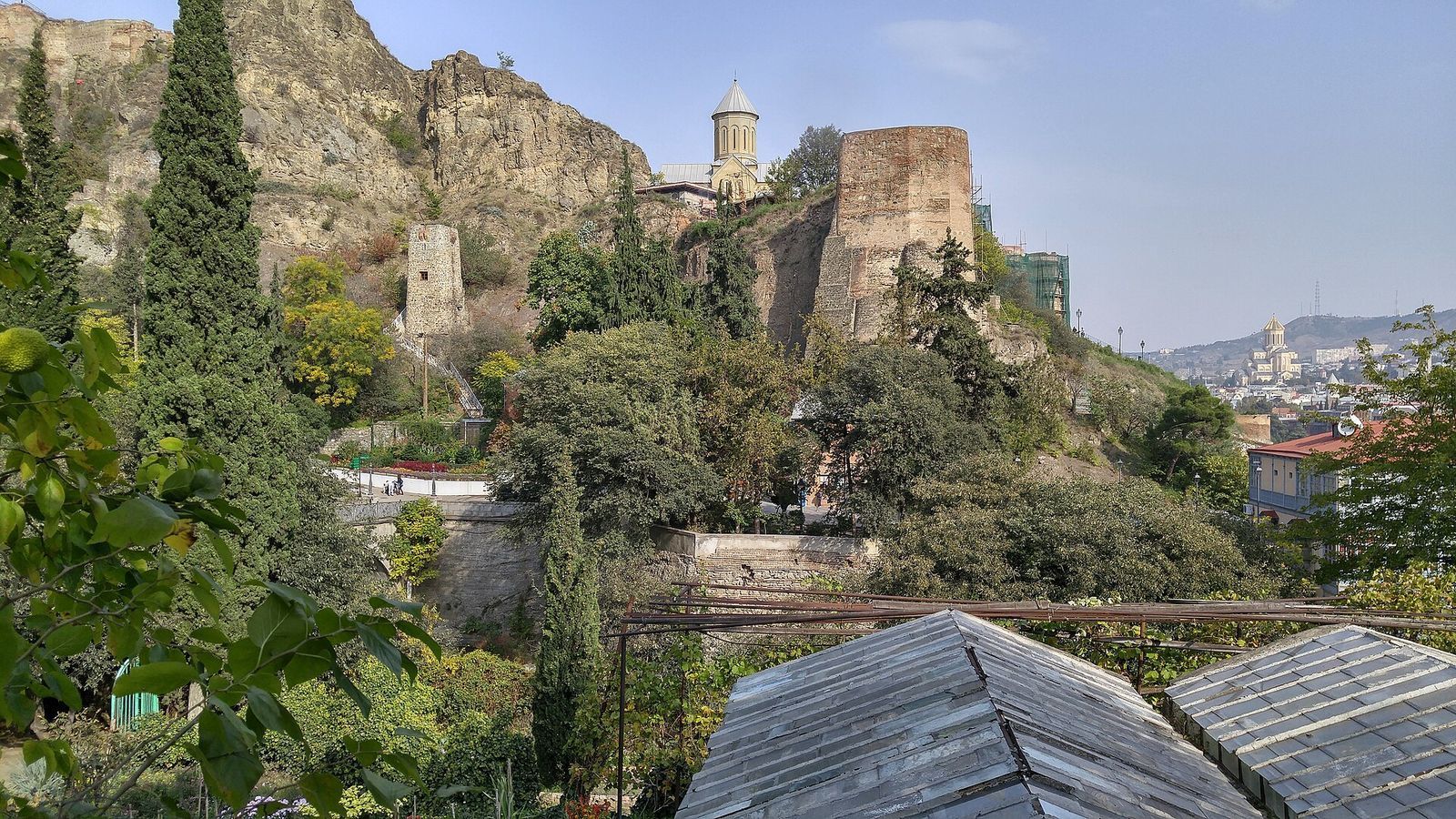 The towers of Narikala fortress and St Nicholas Church on the cliff above the greenhouses of the National Botanical Garden