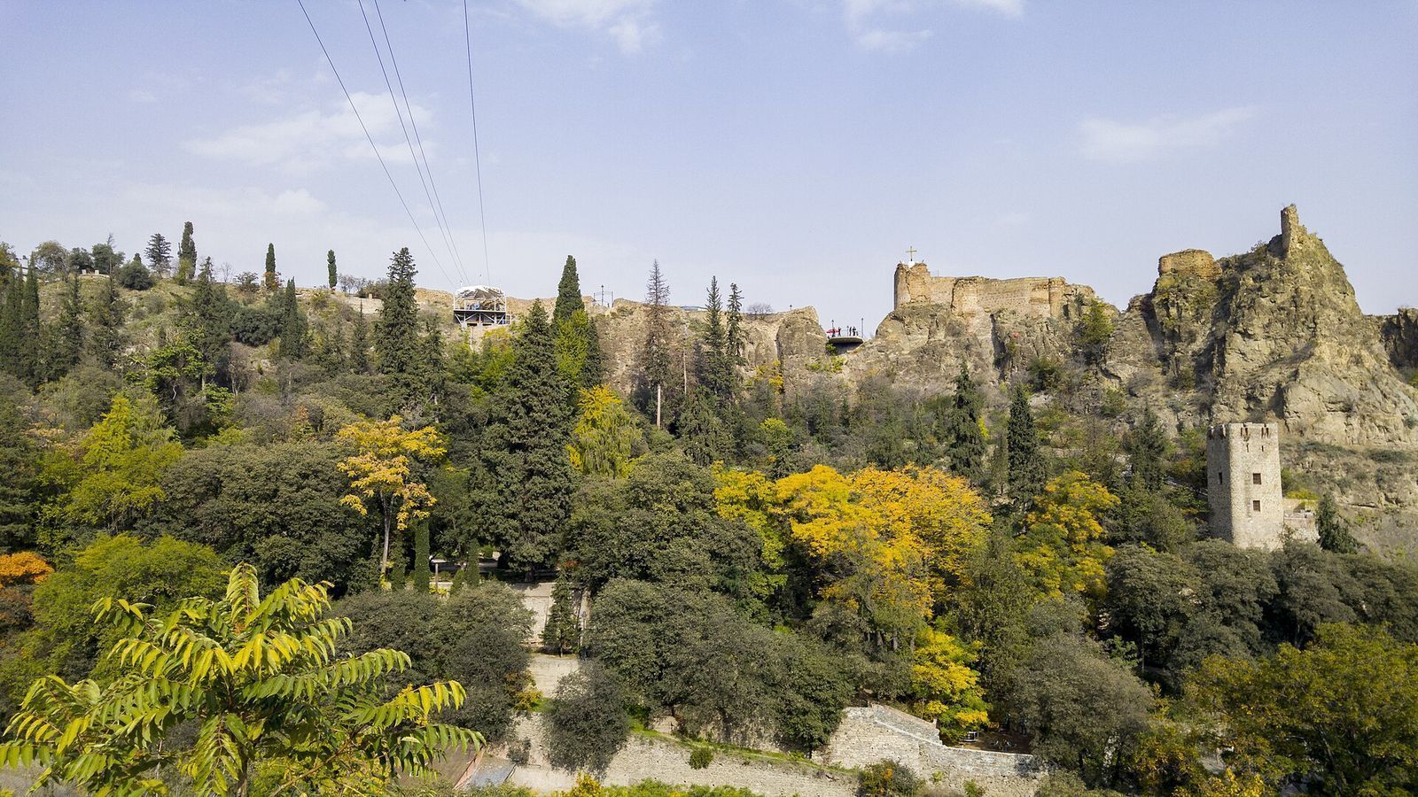 Zip line cables running from the launch platform on the Narikala ridge down over the Botanical Garden, with the fortress walls and a defense tower to the right