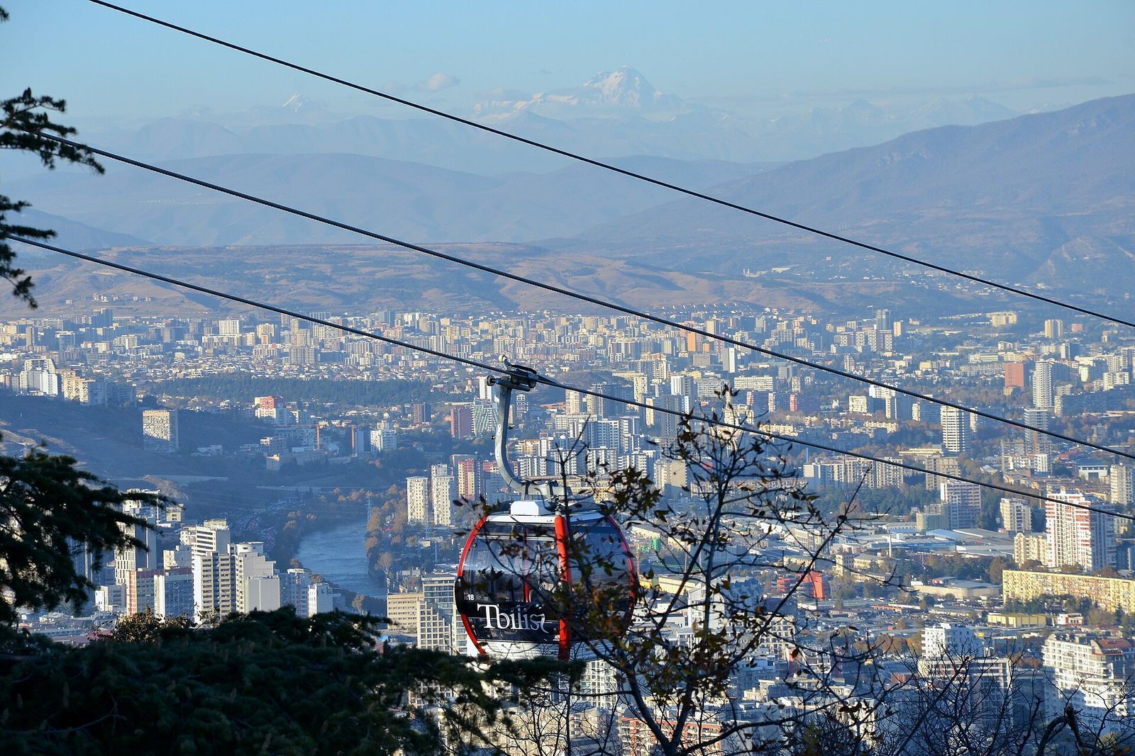 A red Rustaveli to Mtatsminda cable car gondola over Tbilisi, with the Kura river and the city below
