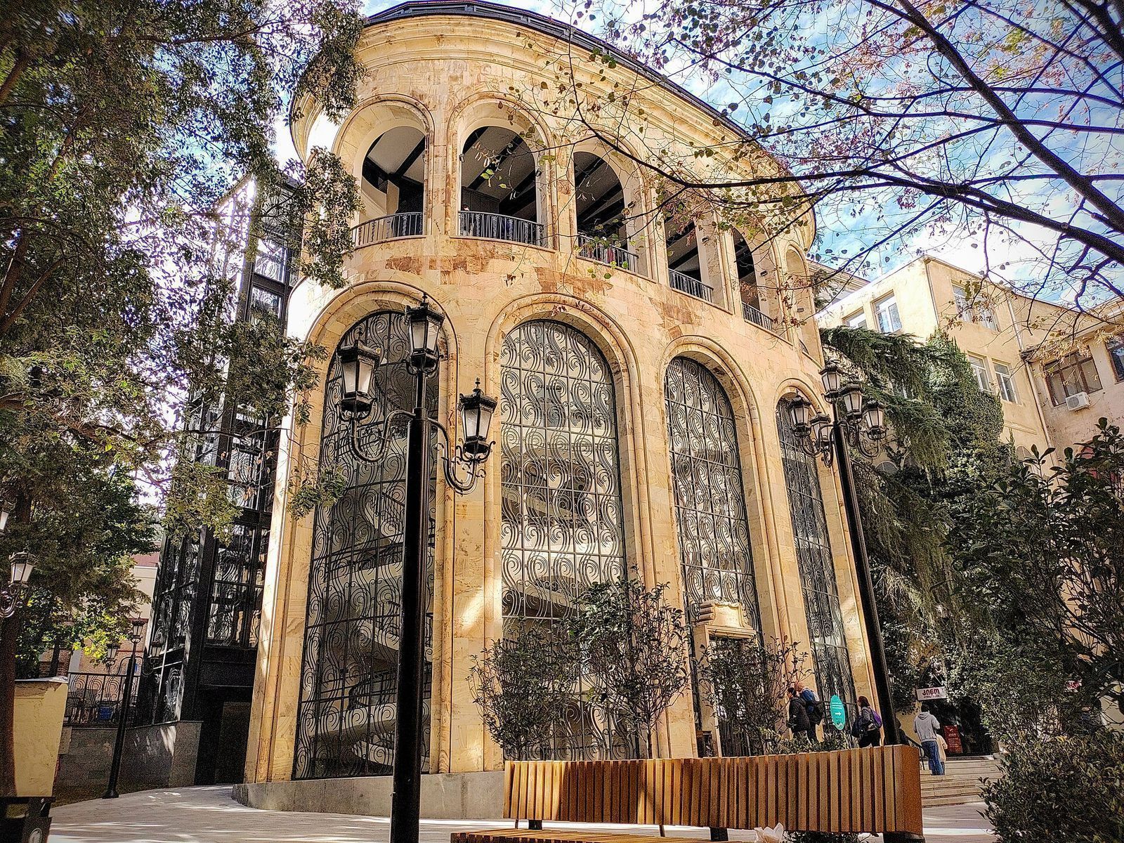 The arched stone ground station of the Rustaveli to Mtatsminda cable car in Tbilisi, framed by trees and street lamps