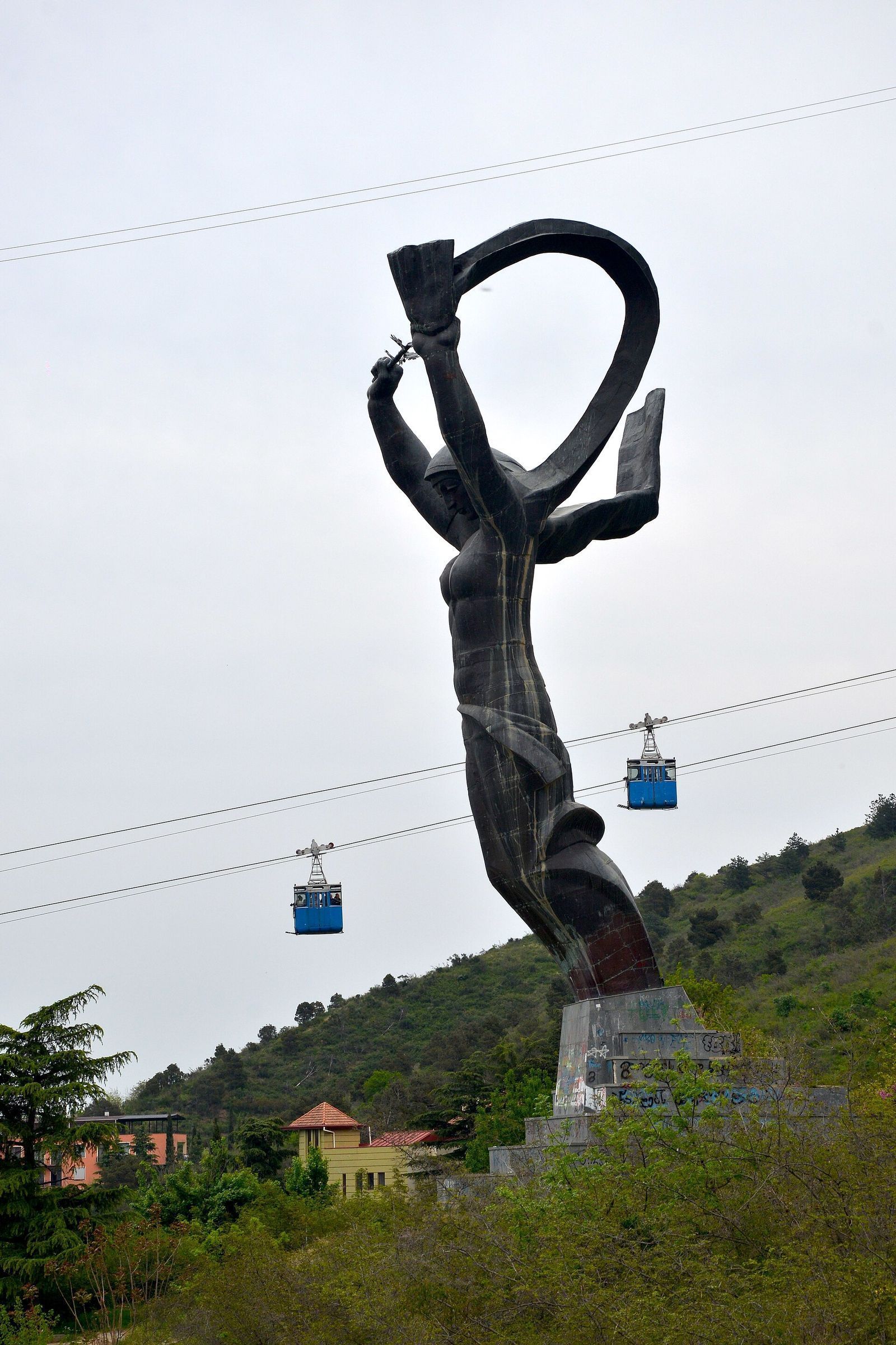 The Victory statue in Vake Park, with blue cable car cabins climbing past it toward Turtle Lake
