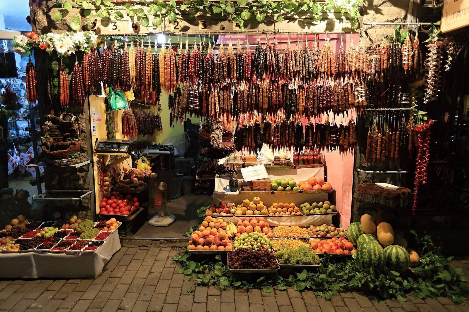 A fruit stall in Old Tbilisi hung with strings of churchkhela above crates of pomegranates, grapes, pears and pumpkins