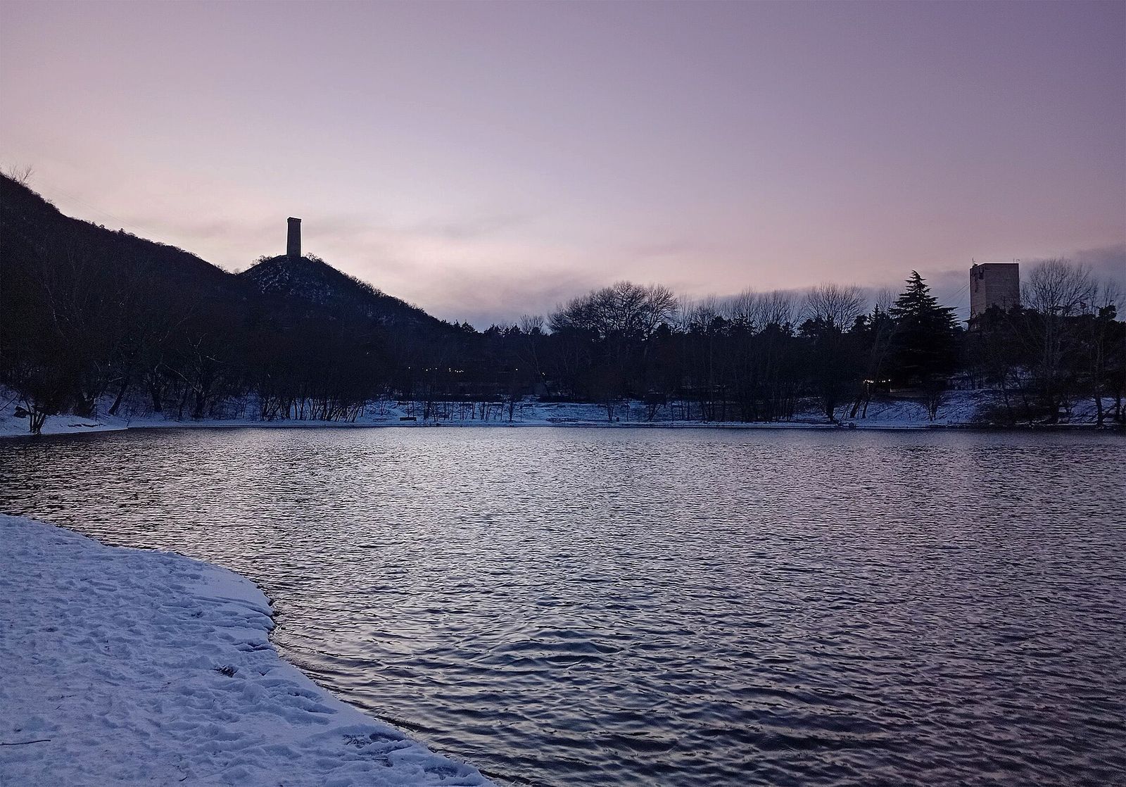 Turtle Lake in Tbilisi at dusk in February, with snow on the shore and the wooded hill behind